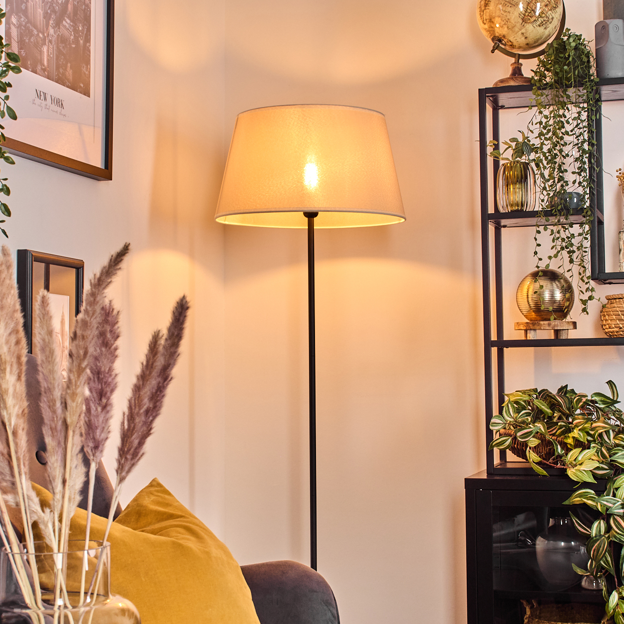 Eine Stehlampe mit beigem Lampenschirm beleuchtet eine gemütliche Wohnzimmerecke.