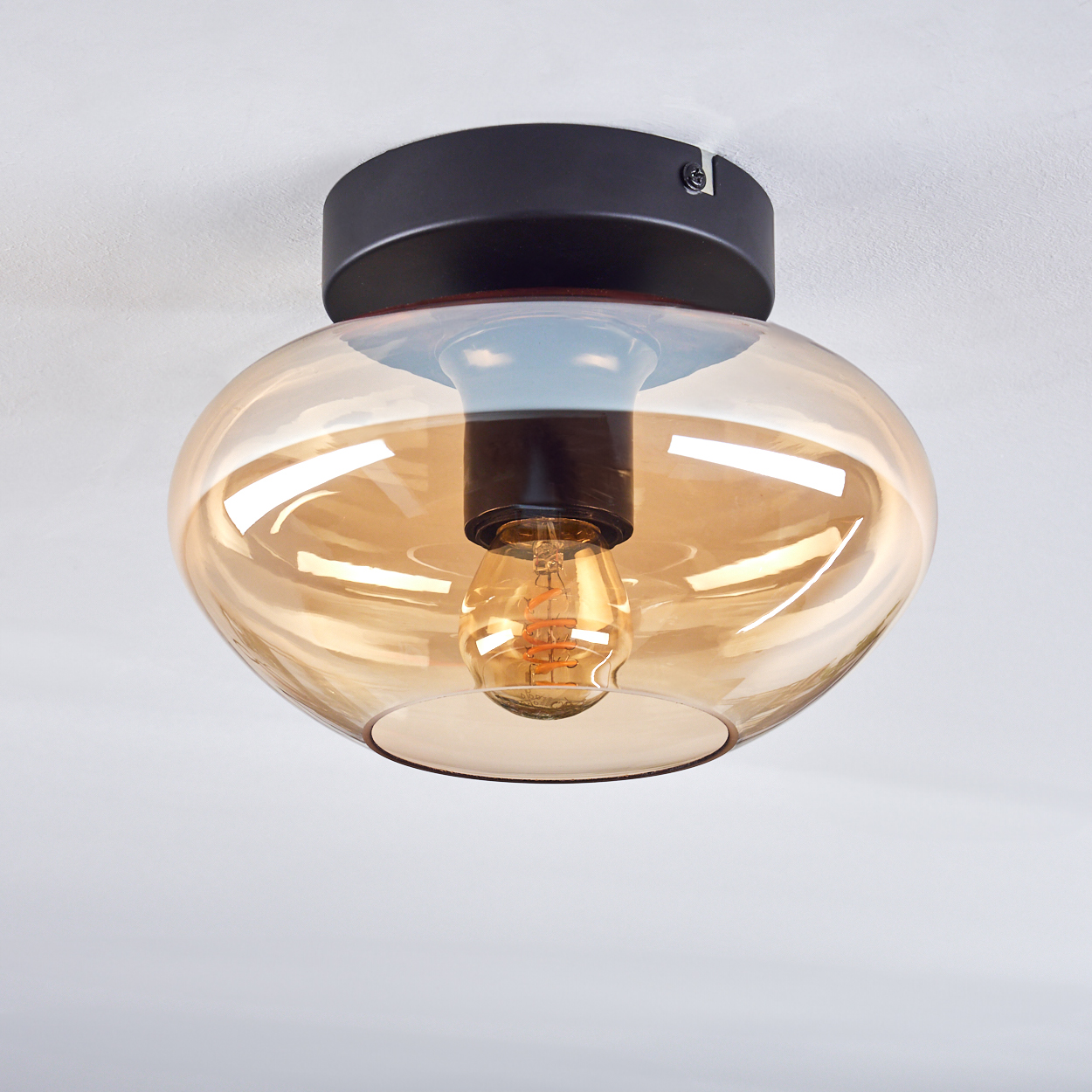 Nahaufnahme einer Deckenlampe mit bernsteinfarbenem Glasschirm und Glühbirne.