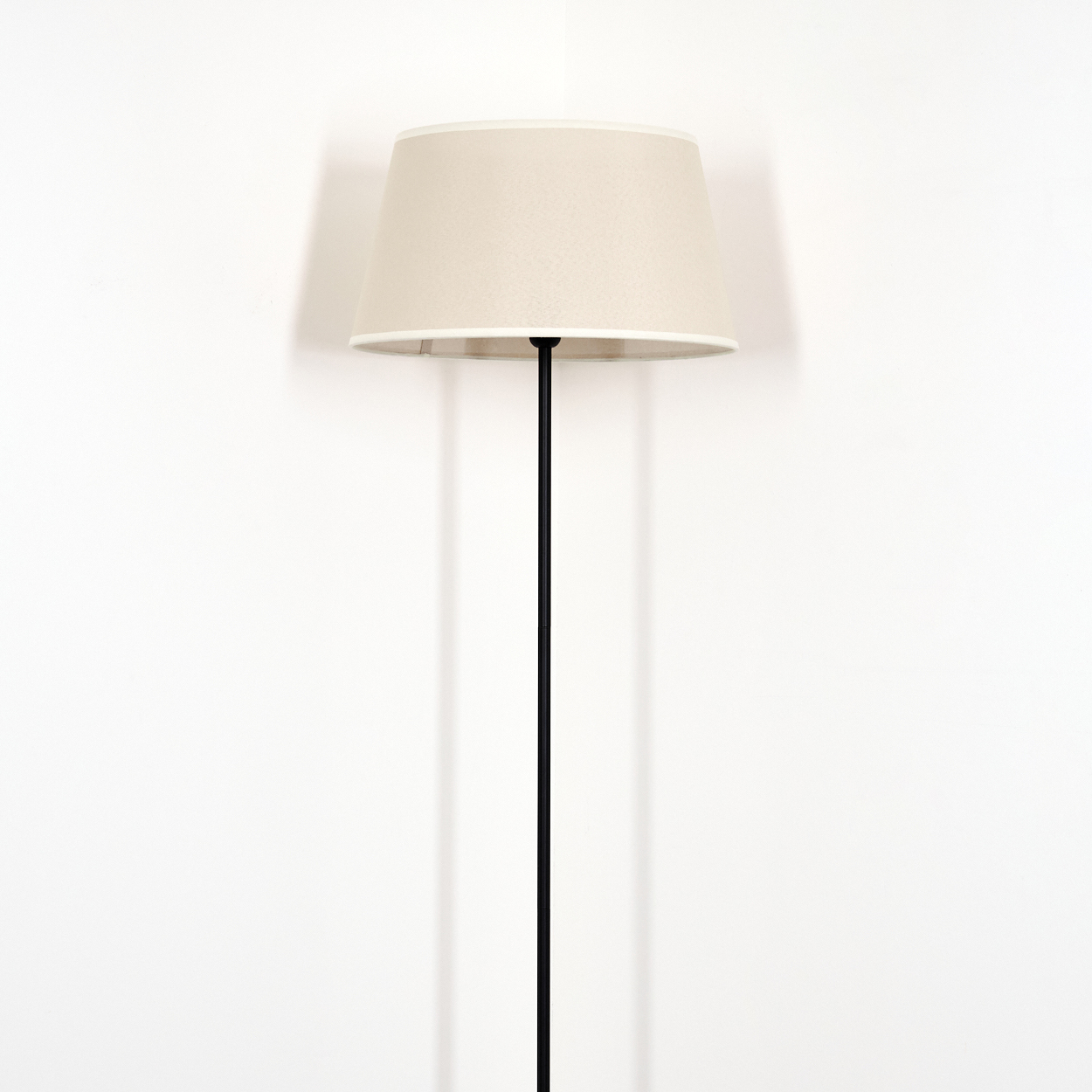 Eine schwarze Lampenstange mit beigem Lampenschirm vor einer weißen Wand.