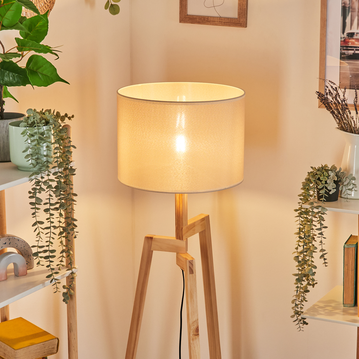 Eine hölzerne Stehlampe mit beleuchtetem beigem Lampenschirm, mit Pflanzen dekoriert.