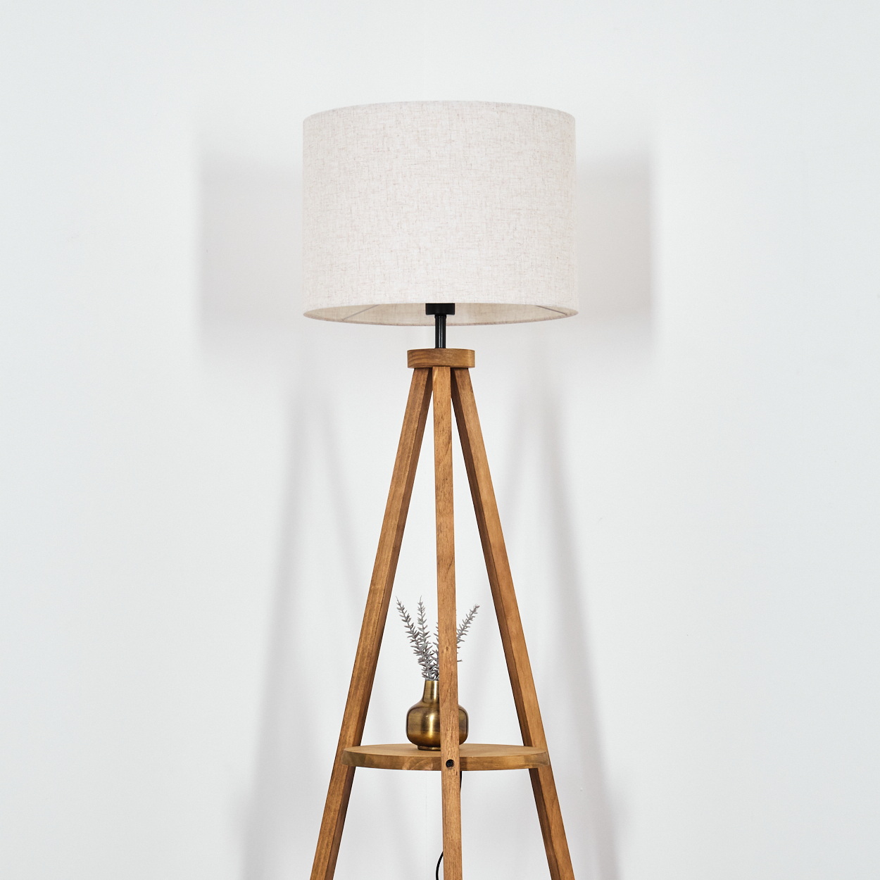 Stehlampe mit beigem Schirm und Holz-Dreibein. Kleine Vase und Deko auf Regal.