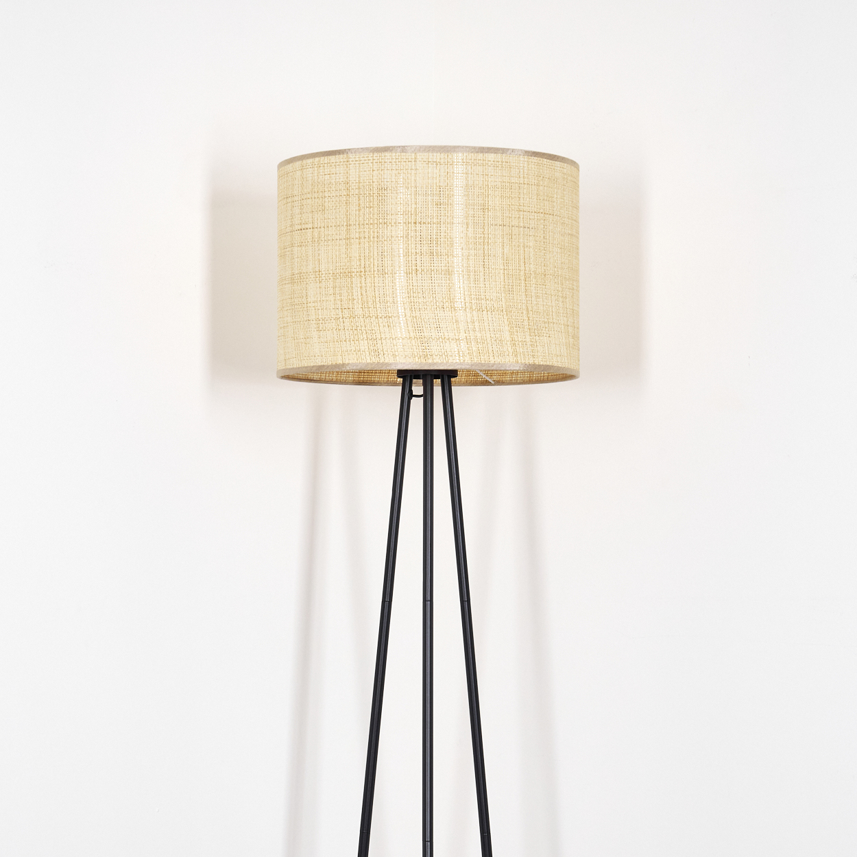 Stehlampe mit gewebtem Schirm und schwarzen Beinen. Weißer Hintergrund und schlichtes Design.