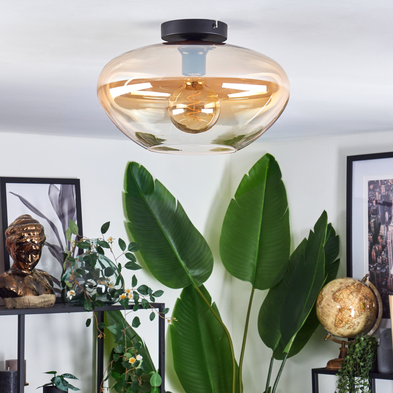 Deckenlampe mit bernsteinfarbenem Glasschirm und Wendel-Glühbirne. Raum mit Pflanzen und Deko.