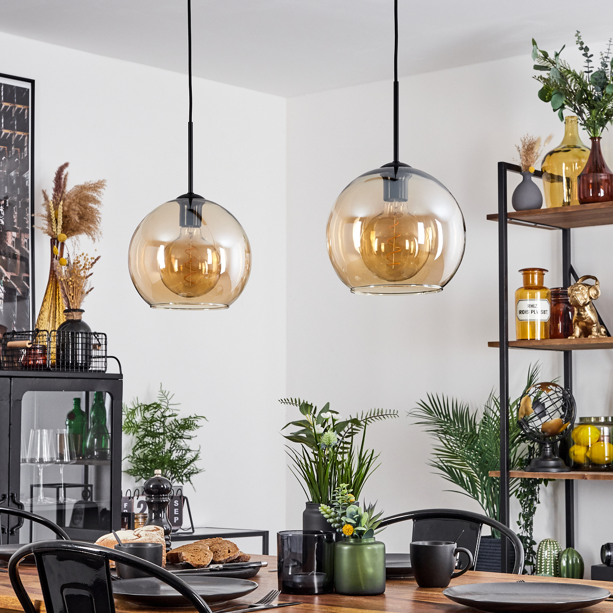 Zwei Pendelleuchten mit bernsteinfarbenen Glasschirmen und sichtbaren Glühbirnen. Esszimmer-Szene.