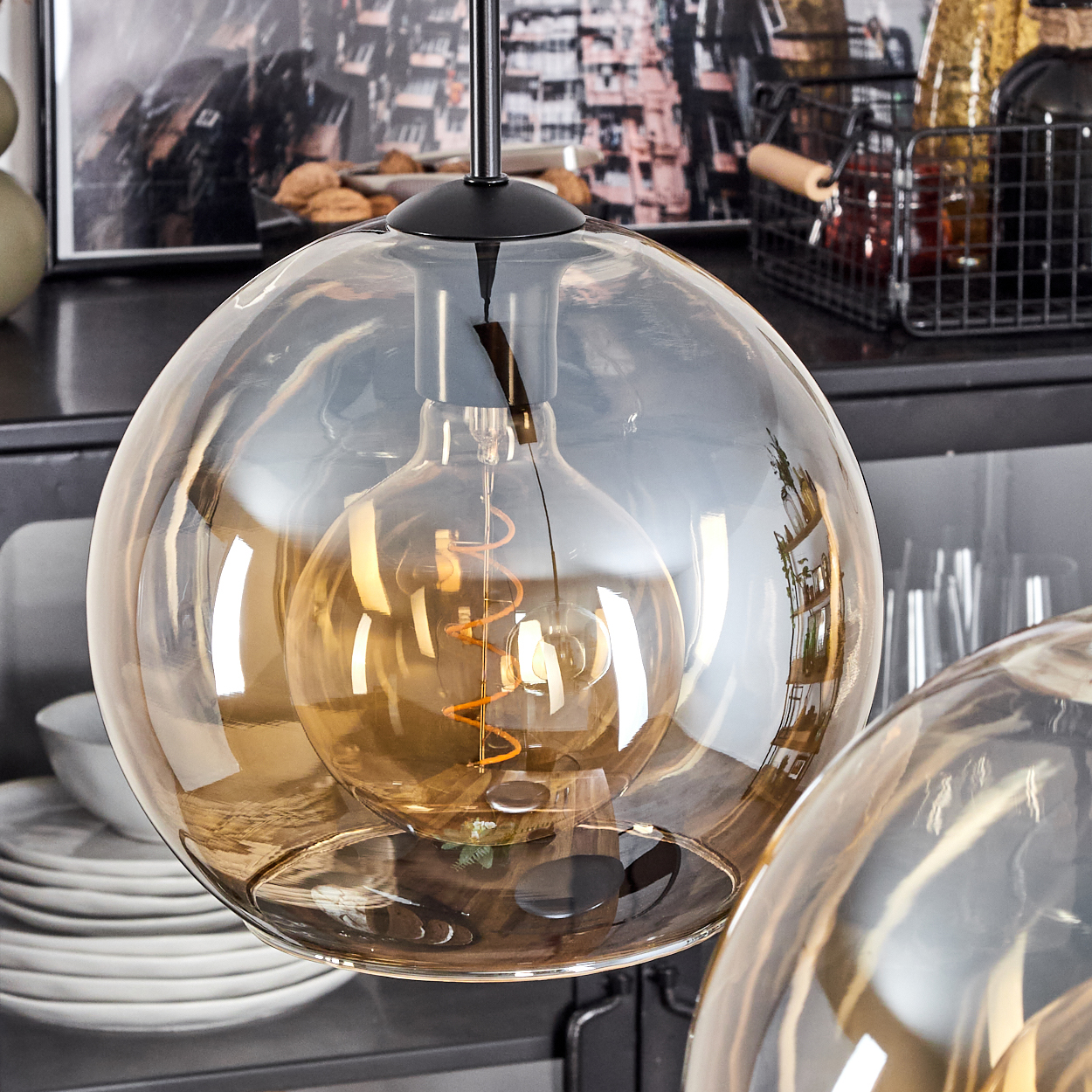 Eine Glas-Pendelleuchte mit sichtbarer Glühbirne. Der Hintergrund hat Regale, Teller und Dekorationsartikel.