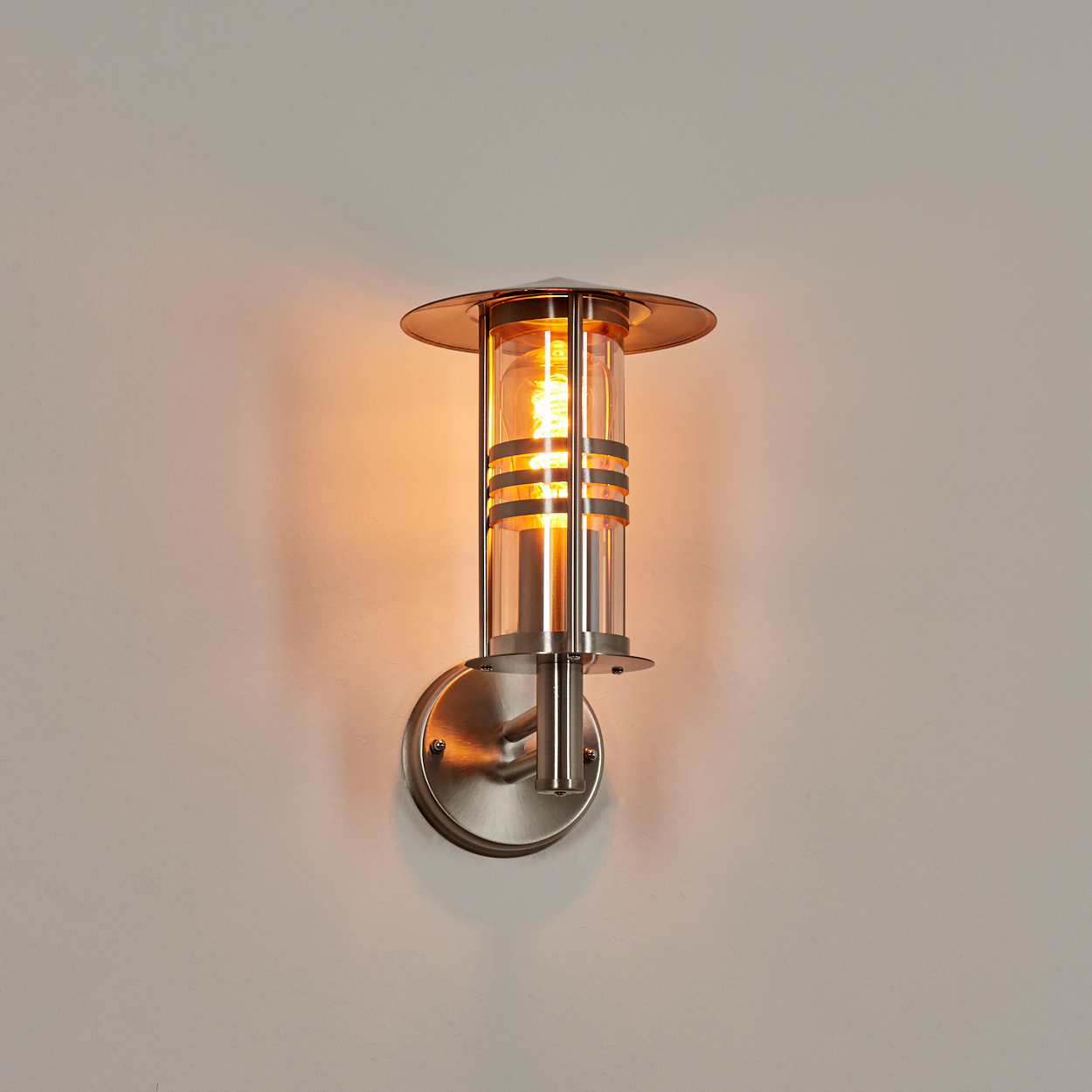 Beleuchtete Außenwandleuchte. Silbernes Metall. Orangefarbene Glühbirne in Zylinderglas.