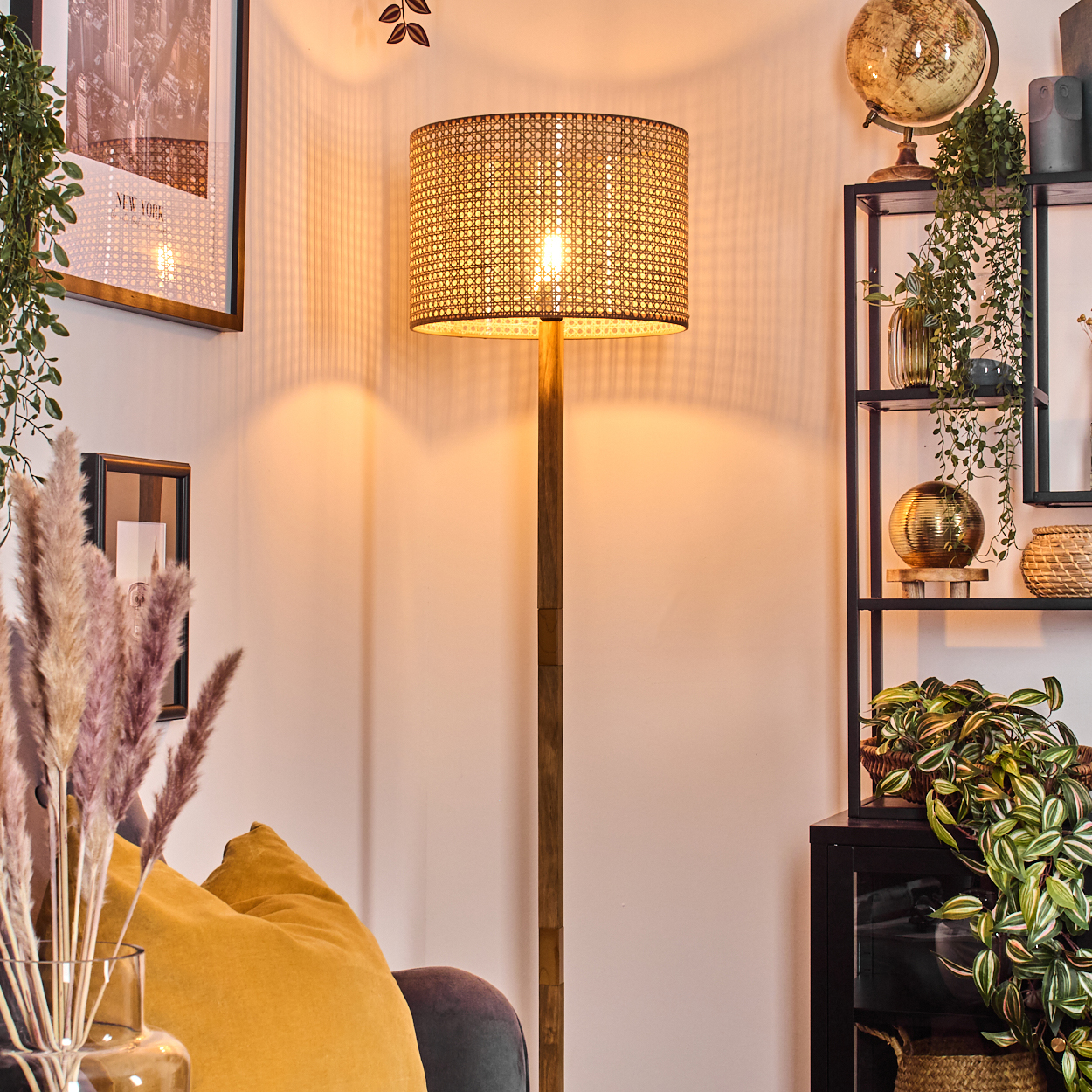 Eine Stehlampe mit gewebtem Schirm, einem schwarzen Regal und Pflanzen in einem Wohnzimmer.