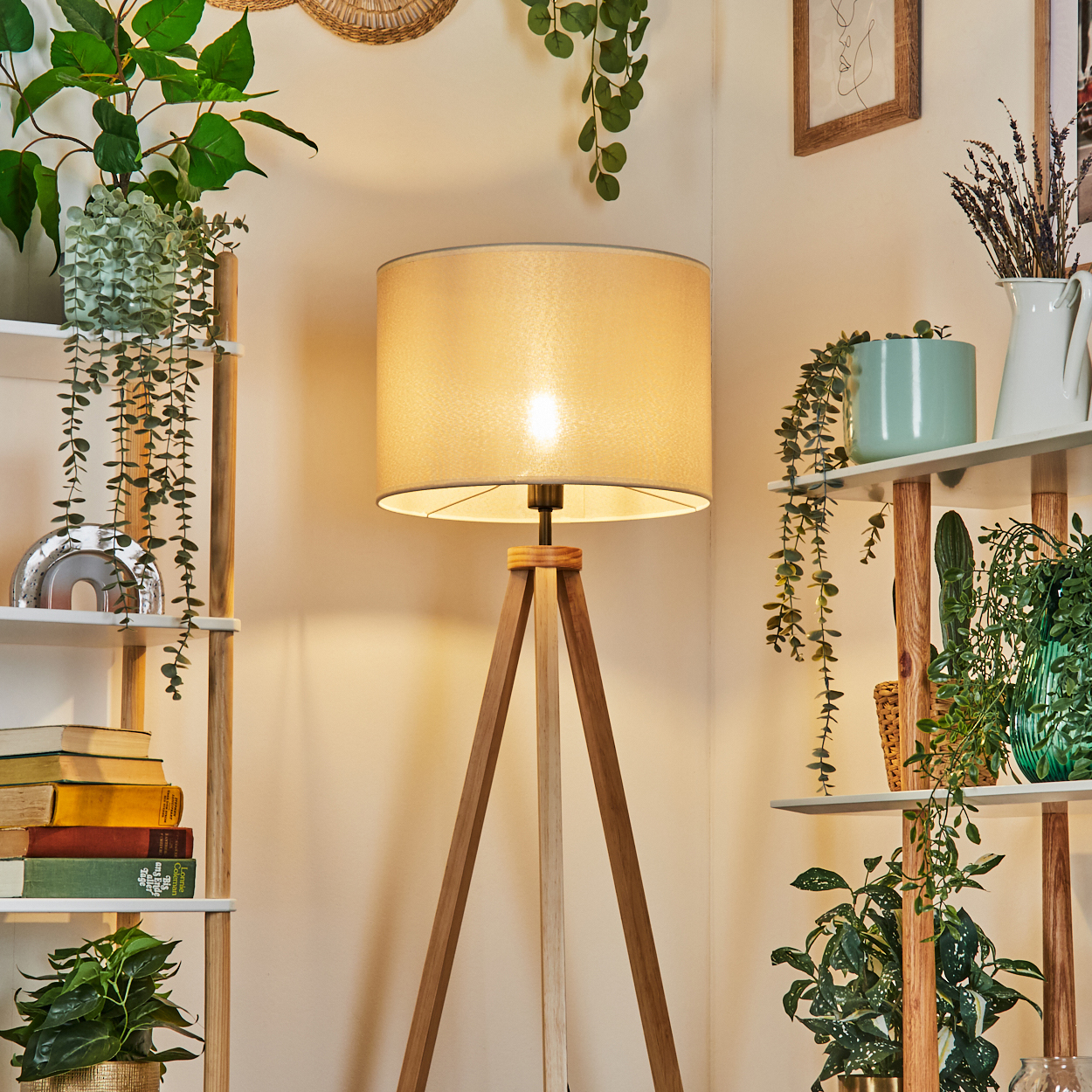 Stehlampe mit beigem Schirm, beleuchtet. Umgeben von Regalen mit Pflanzen und Büchern. Warme Beleuchtung.