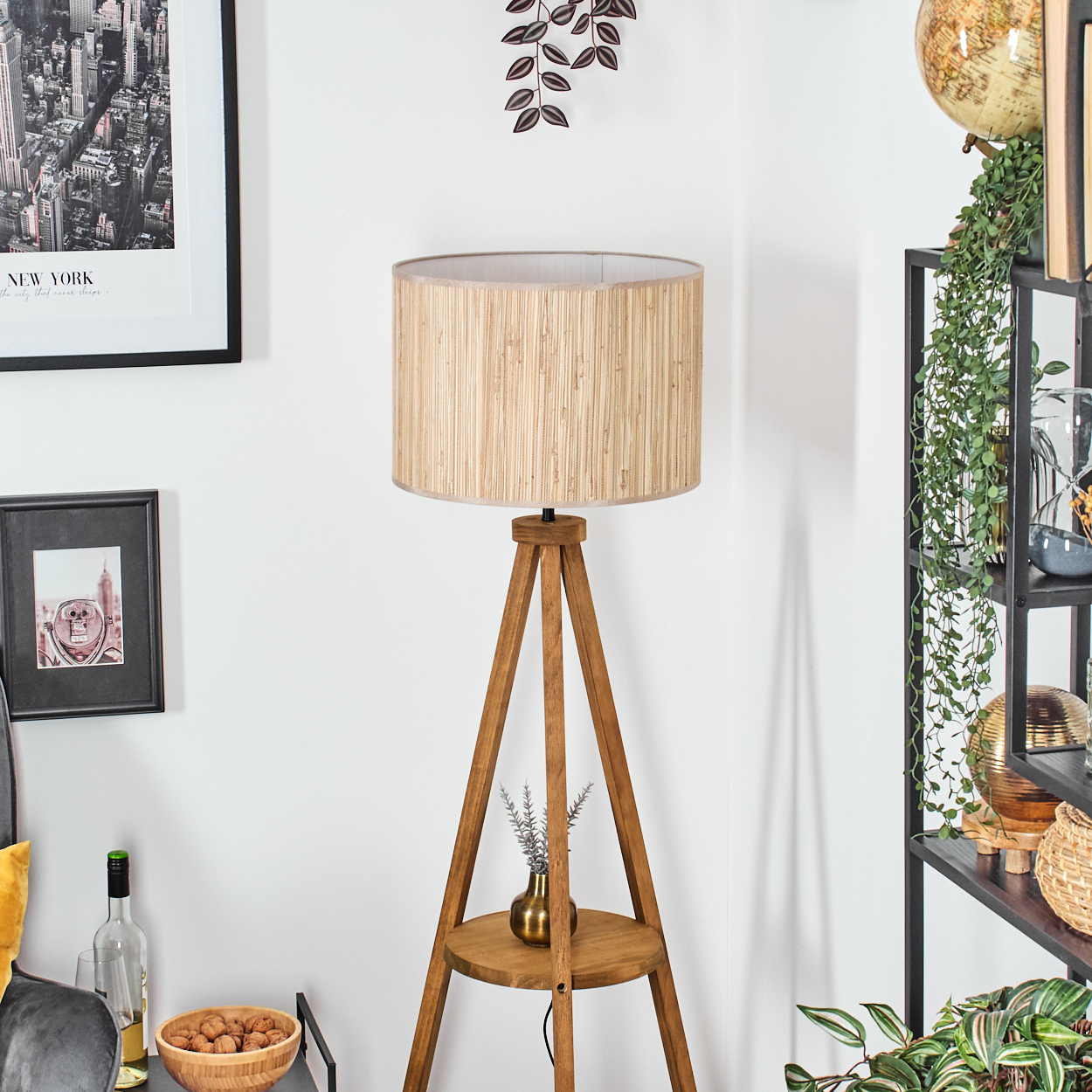 Stativlampe mit Bambus-Schirm, kleiner Tisch. Regal mit Deko und Büchern. Hintergrund mit Kunst.