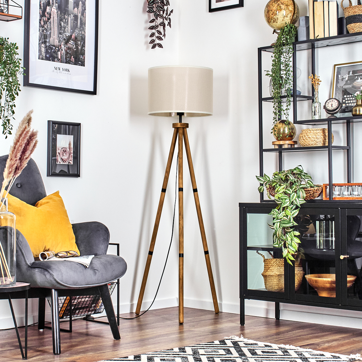 Stativlampe, beiger Schirm, Holzbeine. Stuhl, Kissen und Kunst im Hintergrund.