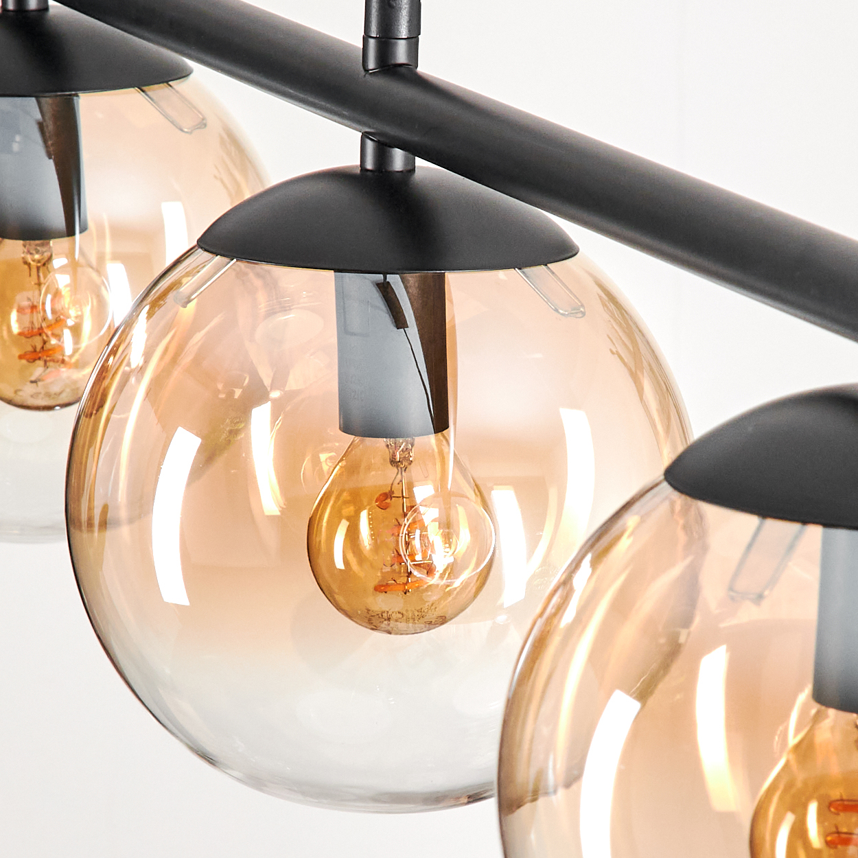 Nahaufnahme einer schwarzen Deckenlampe mit vier bernsteinfarbenen Glaskugeln mit sichtbaren Glühbirnen.