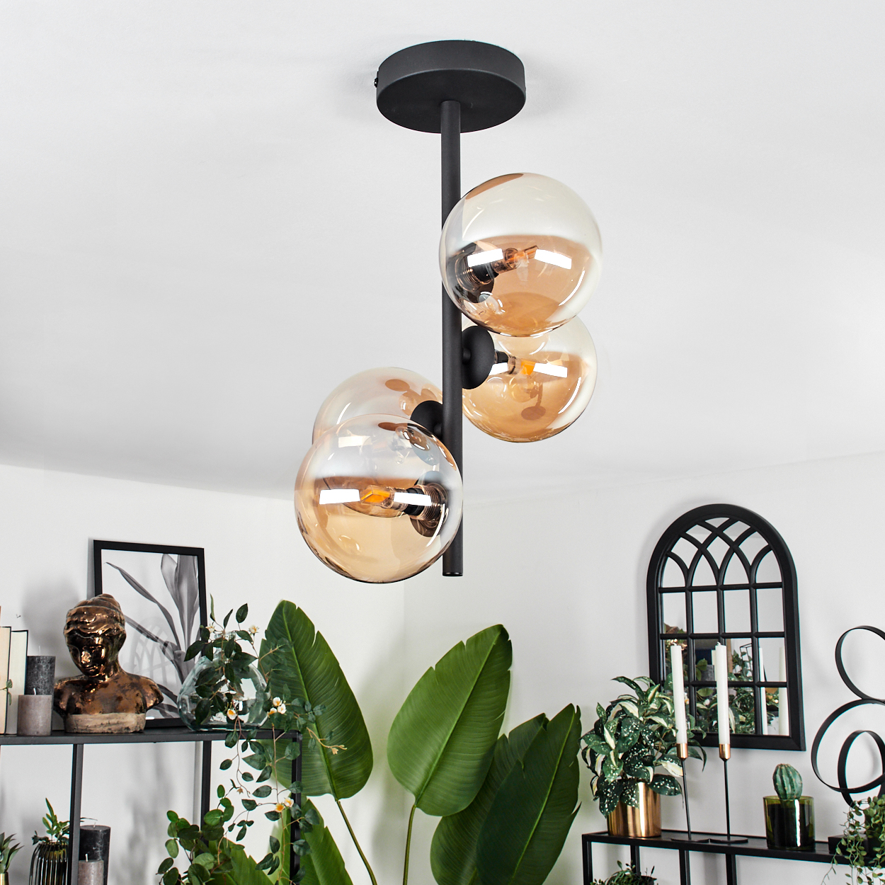 Schwarze moderne Deckenlampe mit vier bernsteinfarbenen Glaskugeln. Weiße Decke, Raum mit Pflanzen und Dekorationen im Hintergrund.