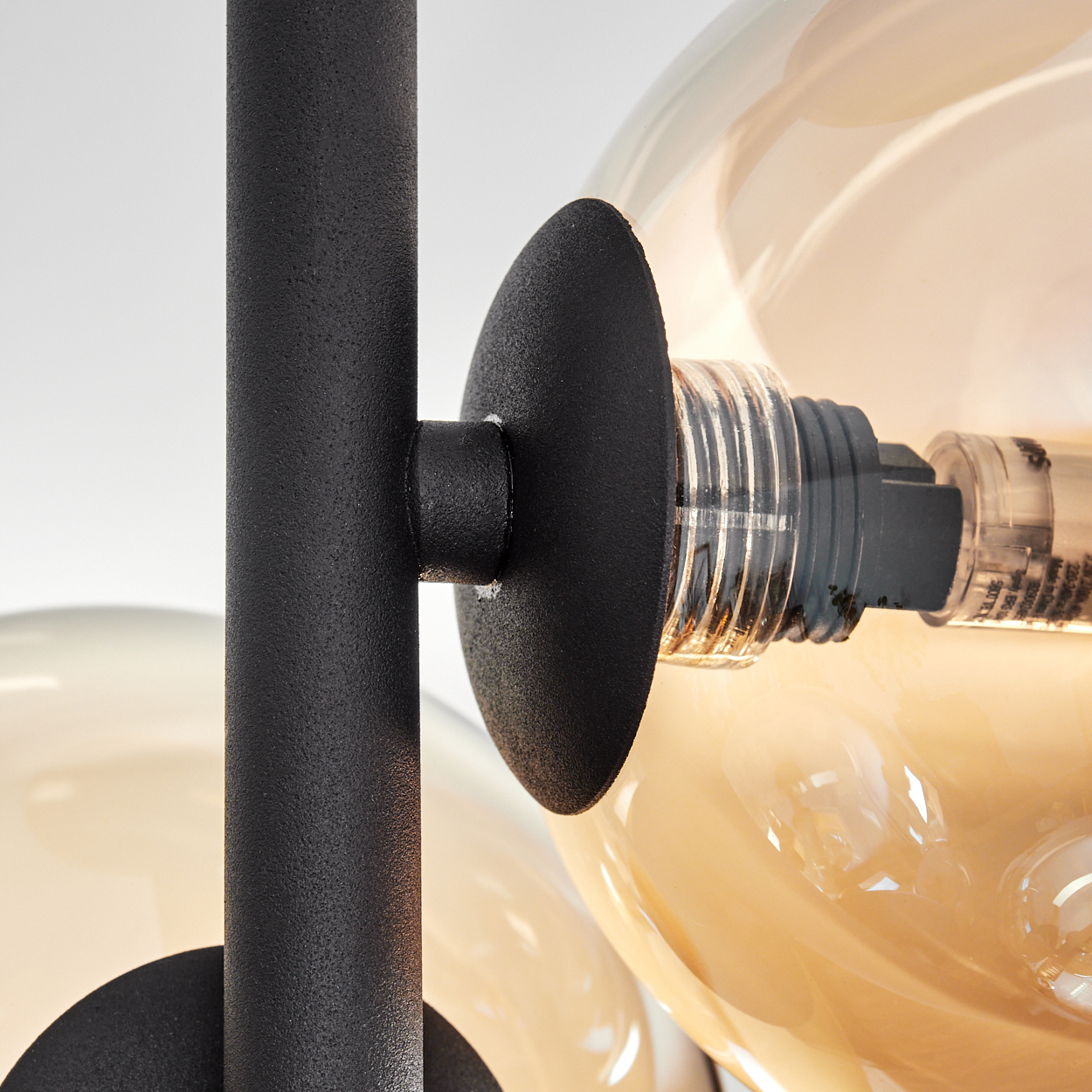 Nahaufnahme einer modernen Lampe mit schwarzen Metallstützen und einer kugelförmigen Glühbirne mit sichtbarem Glühfaden.
