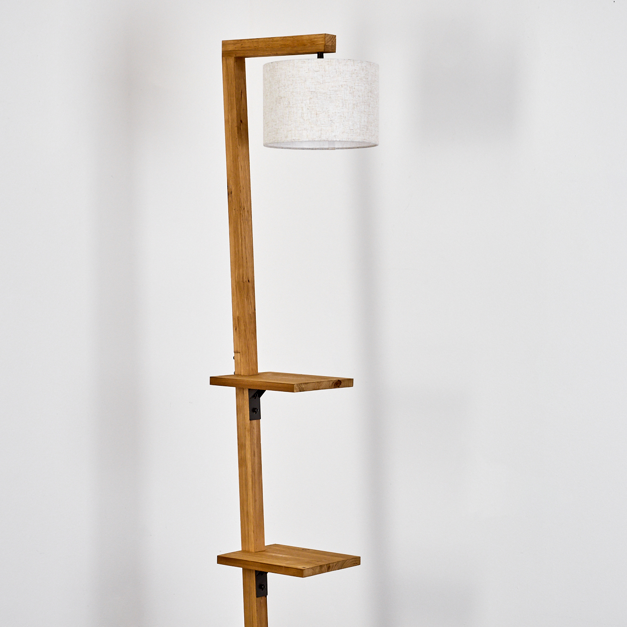 Stehlampe mit Regalen. Heller Holzrahmen mit zwei Regalen. Die Lampe steht vor einer weißen Wand.