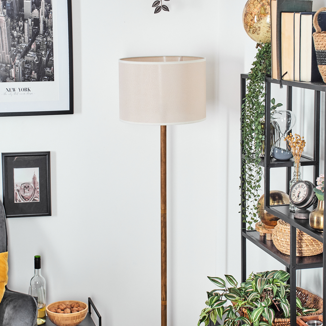 Stehlampe mit beigem Schirm und Holzstange, Deko im Hintergrund.