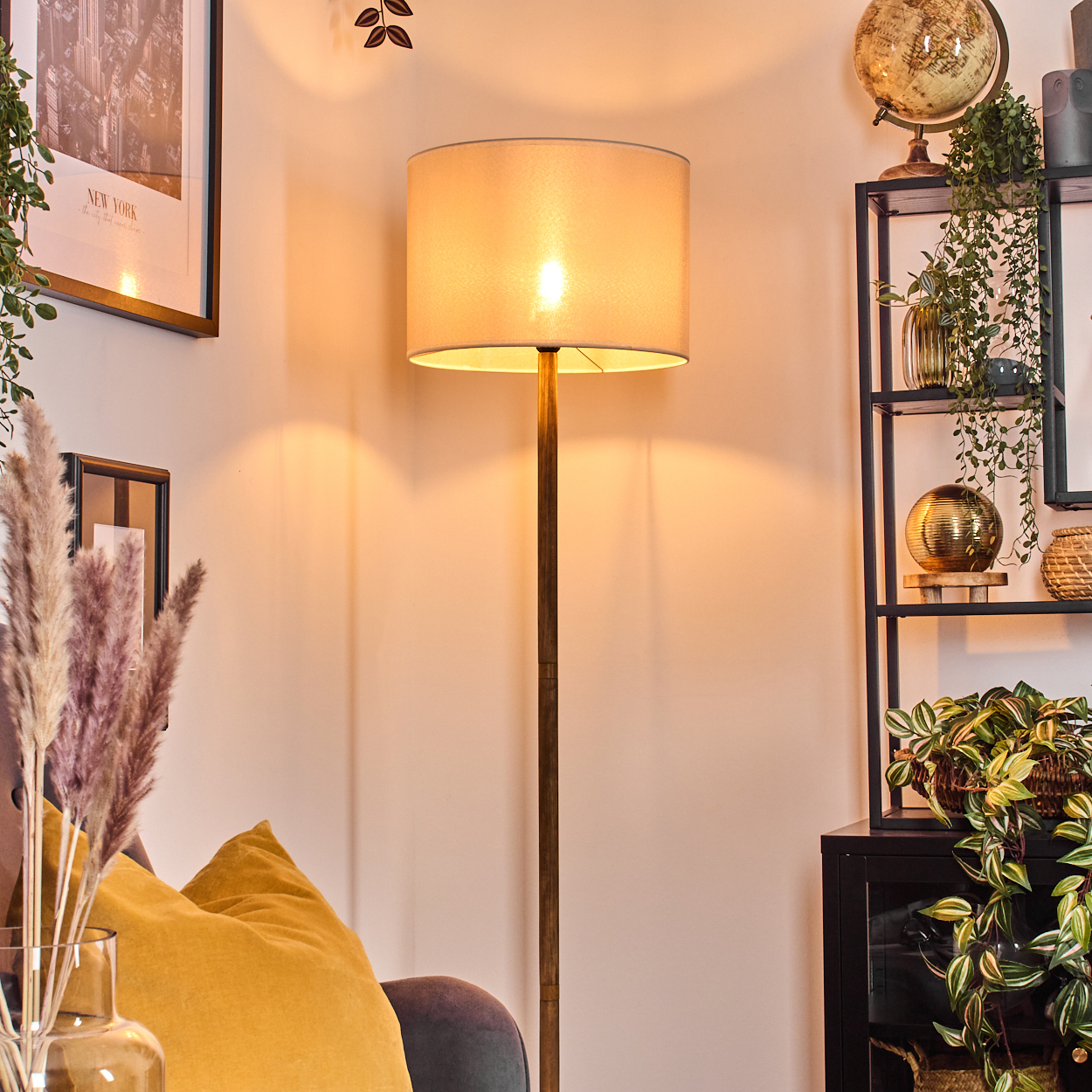 Stehlampe mit beigem Lampenschirm. Inneneinrichtung mit Pflanzen und Regalen.