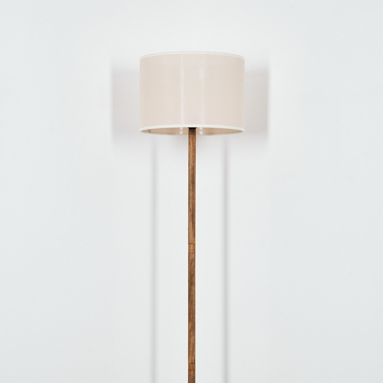 Stehlampe, Holzstange mit beigem Schirm. Weißer Wandhintergrund. Schlichtes, elegantes Design.
