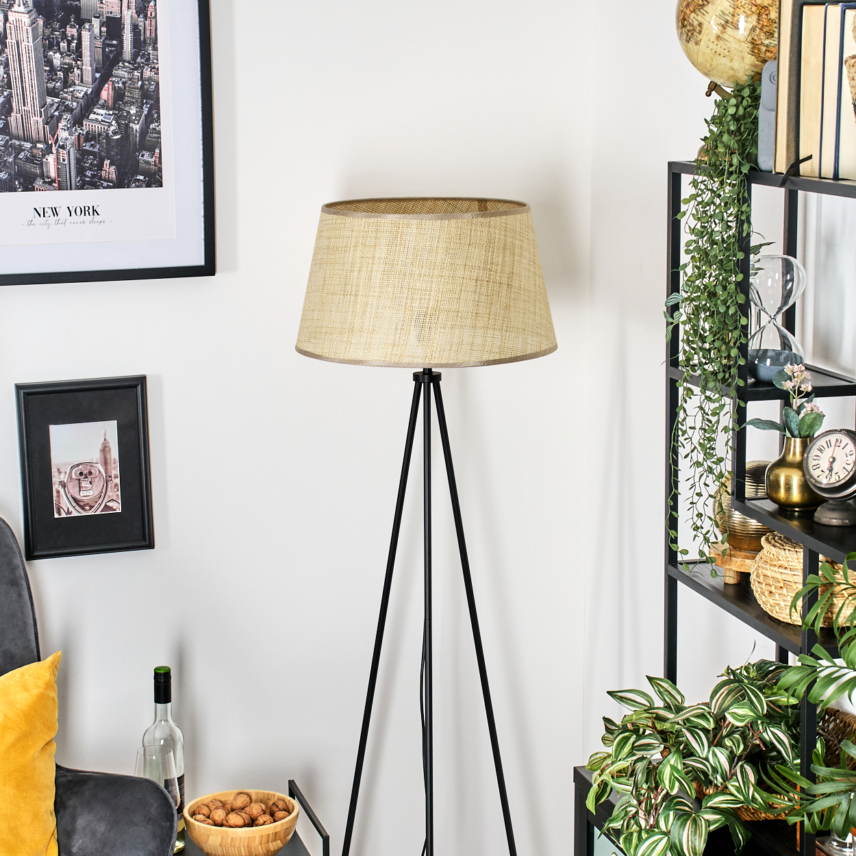 Dreibein-Stehlampe mit beigem Lampenschirm, Inneneinrichtung mit Regalen und Pflanzen.