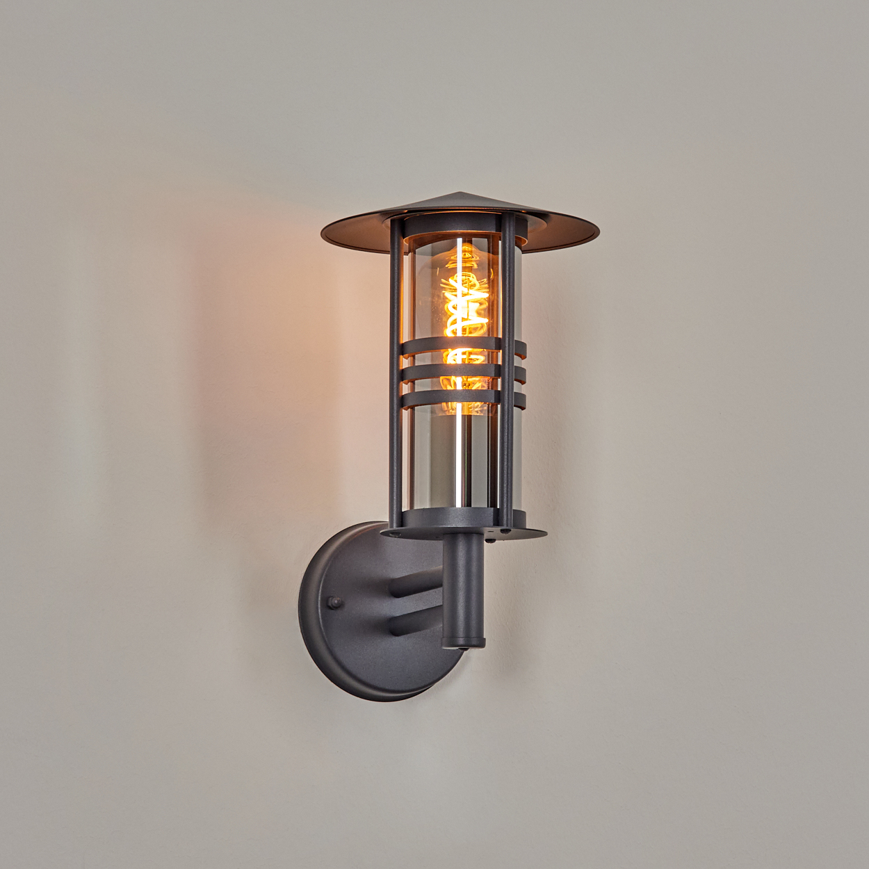 Außenwandleuchte, dunkelgrau mit zylindrischem Design, beleuchtet.
