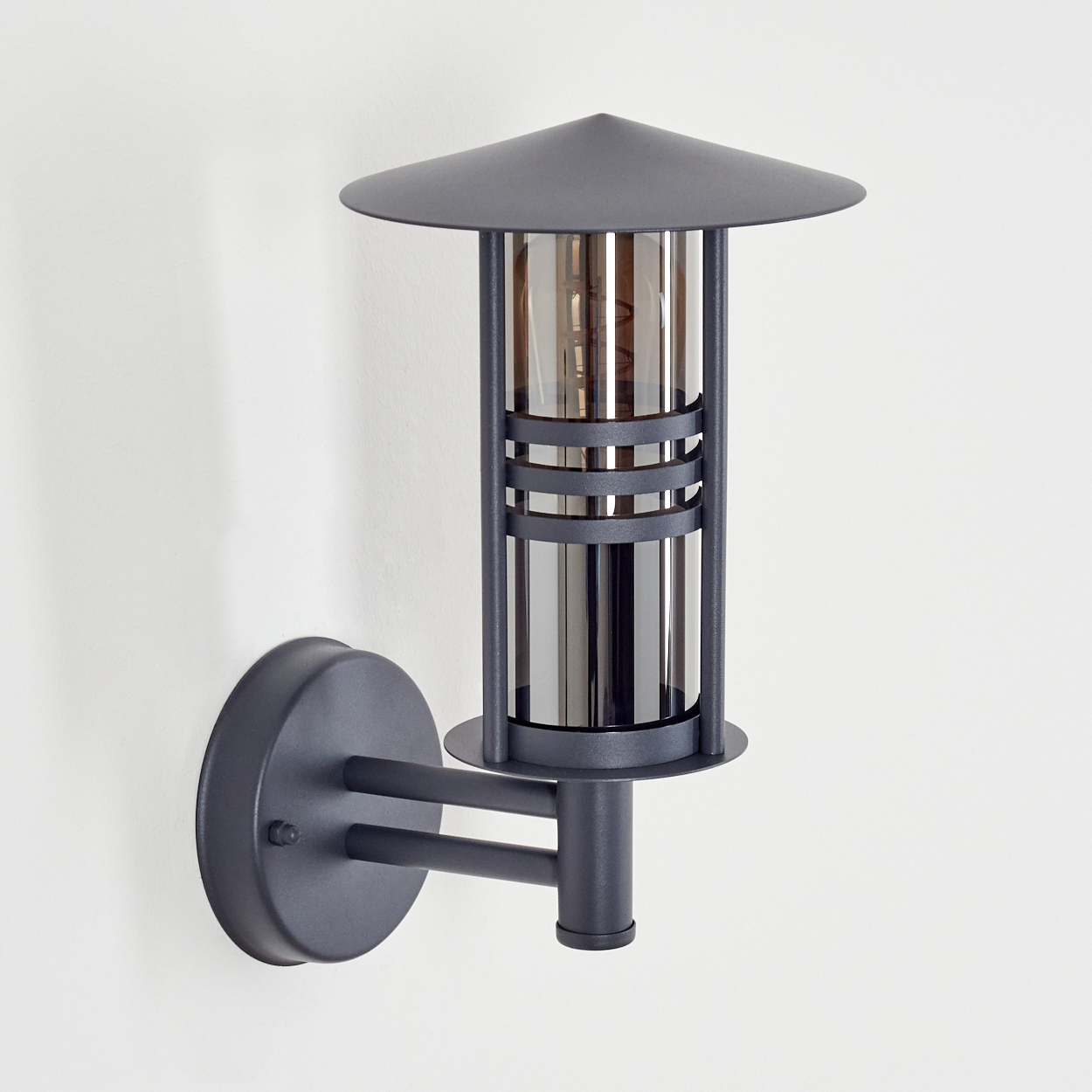 Eine Außenlampe an einer weißen Wand. Sie hat ein zylindrisches Design mit konischem Aufsatz.