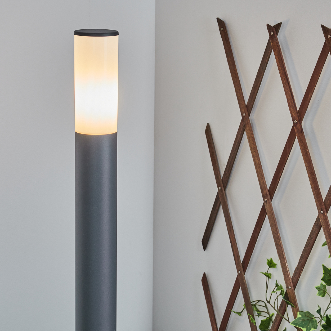 Außenlampe mit leuchtendem Oberteil, neben einem Holzspalier mit grünem Efeu.