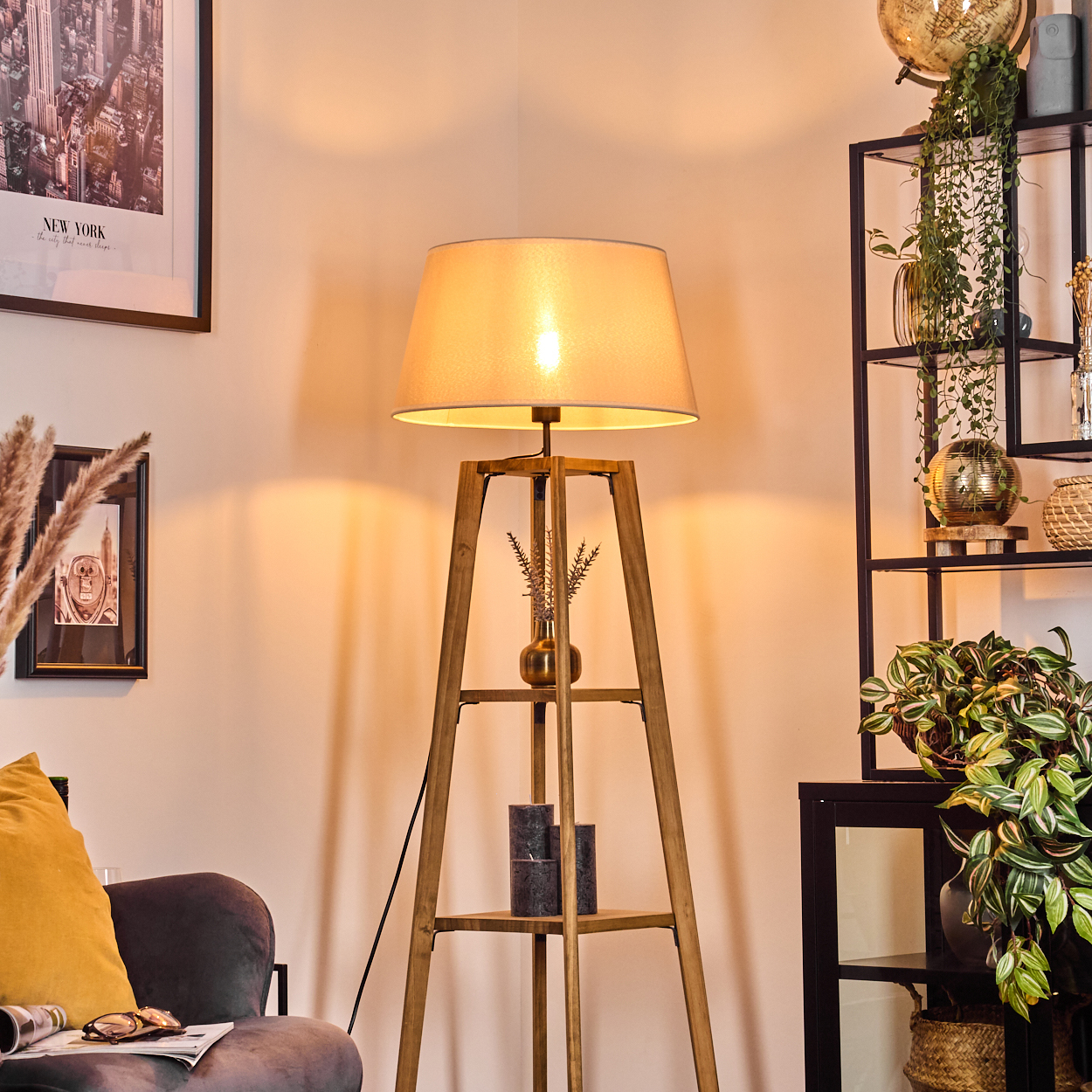 Stehlampe mit beigem Schirm, beleuchtet, in einem Raum. Hintergrund Regal und Deko.