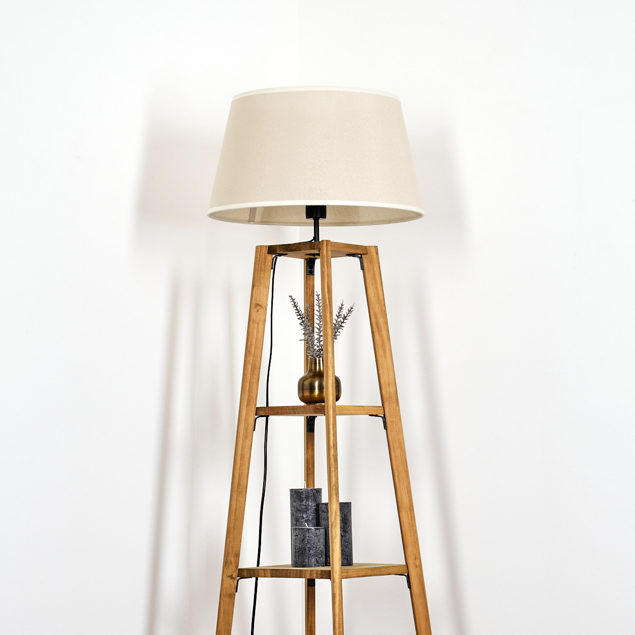 Stehlampe mit beigem Lampenschirm, beleuchtet. In einer Ecke platziert. Vasen und Kerzen auf Regalen.