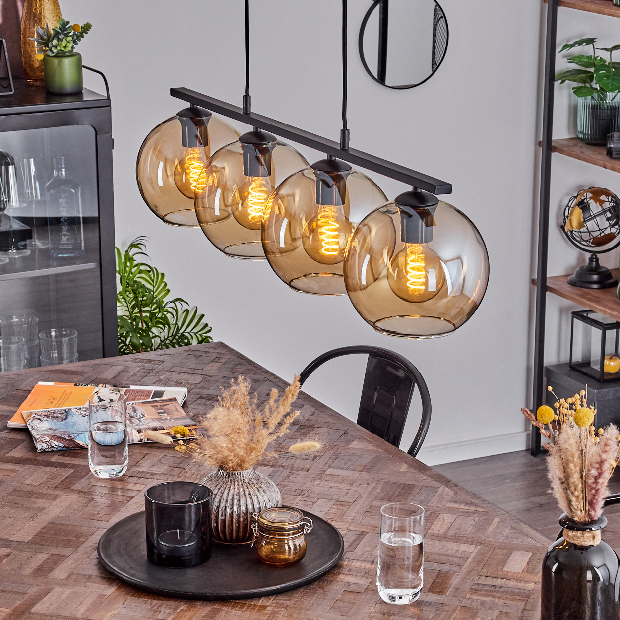 Raum mit vier bernsteinfarbenen Glas-Kugel-Pendelleuchten über einem Holztisch. Andere Deko sichtbar.