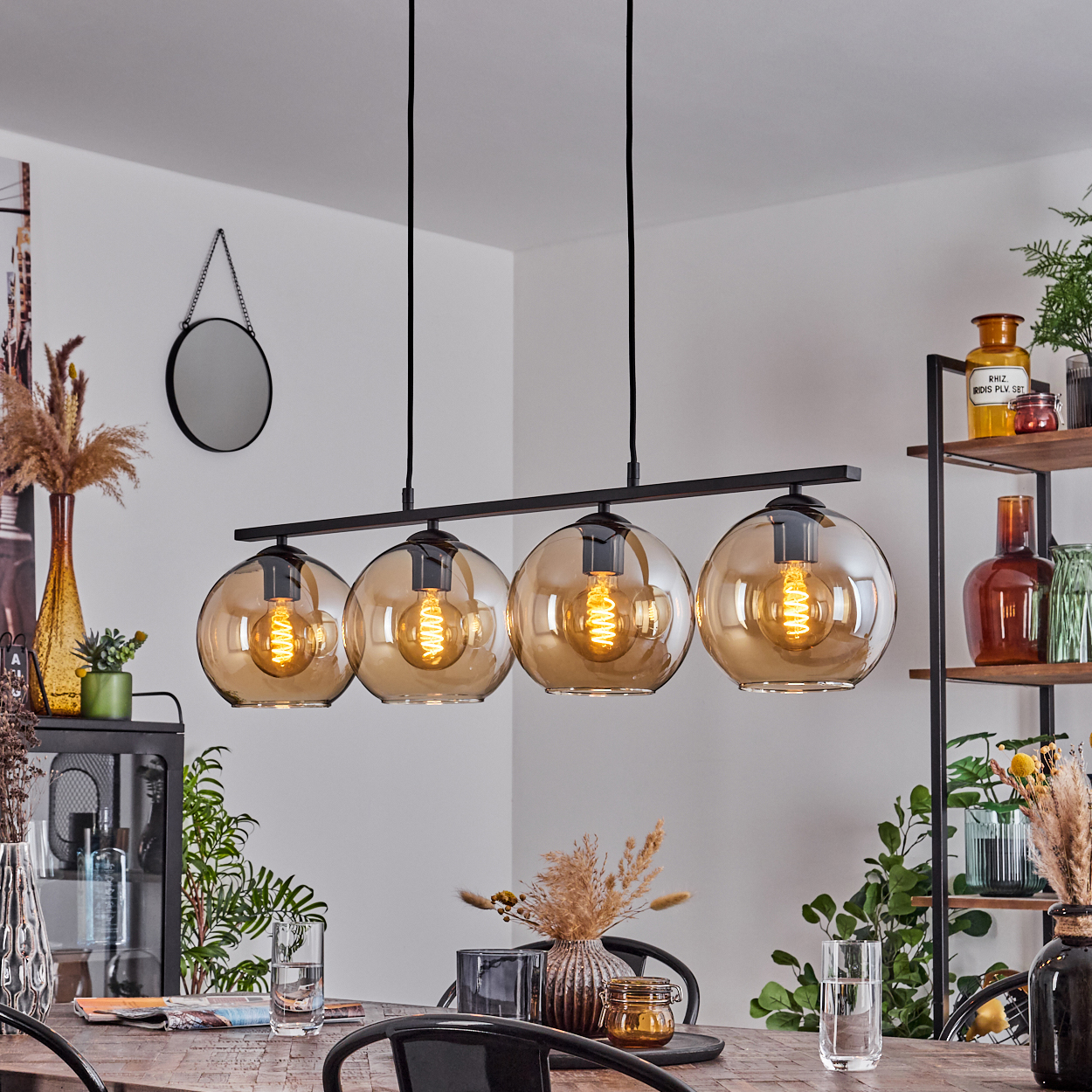 Esszimmer mit einer vierflammigen Pendelleuchte über einem Holztisch, Vase und Dekor auf den Regalen.