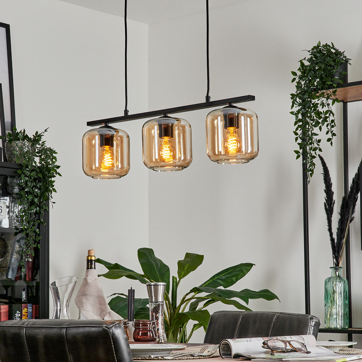 Esszimmer mit Dreifachleuchte, bernsteinfarbenen Glasschirmen und einem Tisch mit Dekoration.
