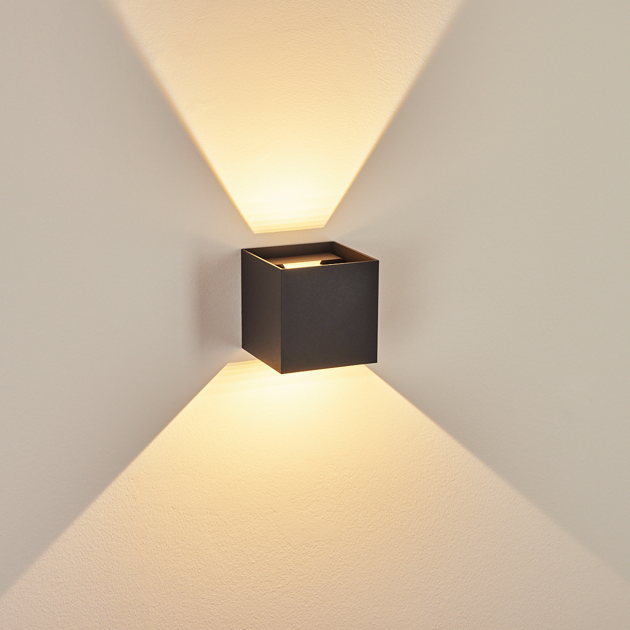 Quadratische, schwarze Außenleuchte an einer weißen Wand, die zwei Lichtstrahlen nach oben und unten projiziert.