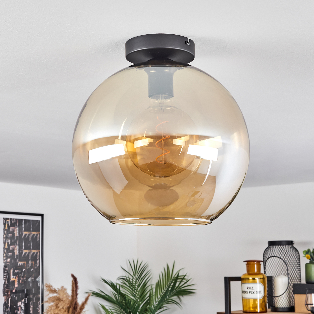 Eine Deckenleuchte mit einem kugelförmigen, bernsteinfarbenen Glasschirm mit einer sichtbaren Glühbirne.