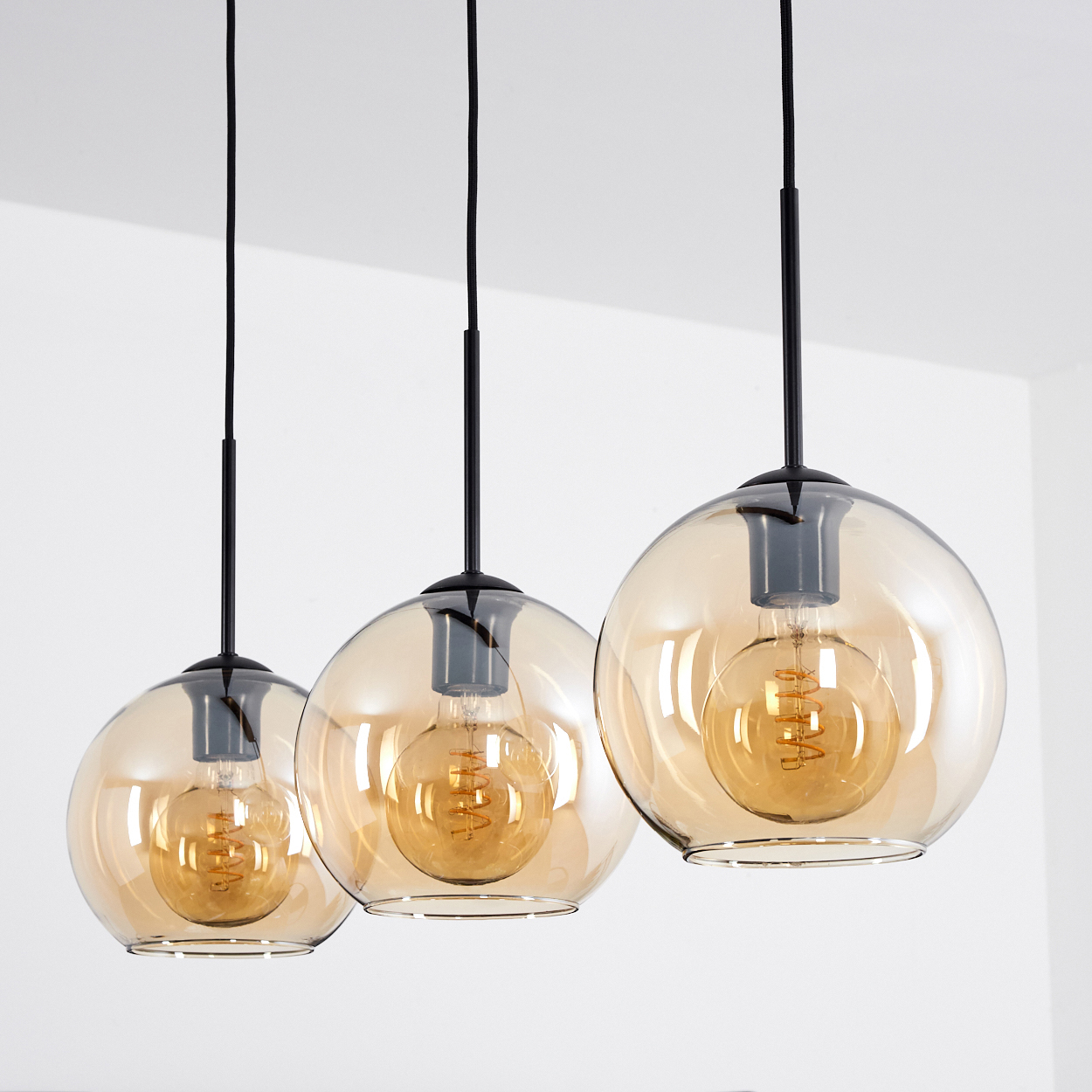 Drei bernsteinfarbene Glas-Pendelleuchten mit Edison-Glühbirnen vor weißem Hintergrund. Die Glühbirnen sind beleuchtet.