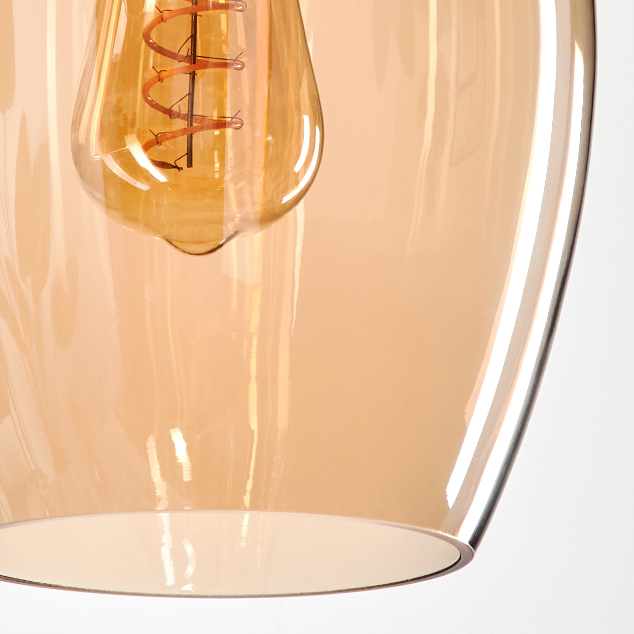Nahaufnahme einer beleuchteten Edison-Glühbirne in einer bernsteinfarbenen Glas-Pendelleuchte. Weißer Hintergrund.