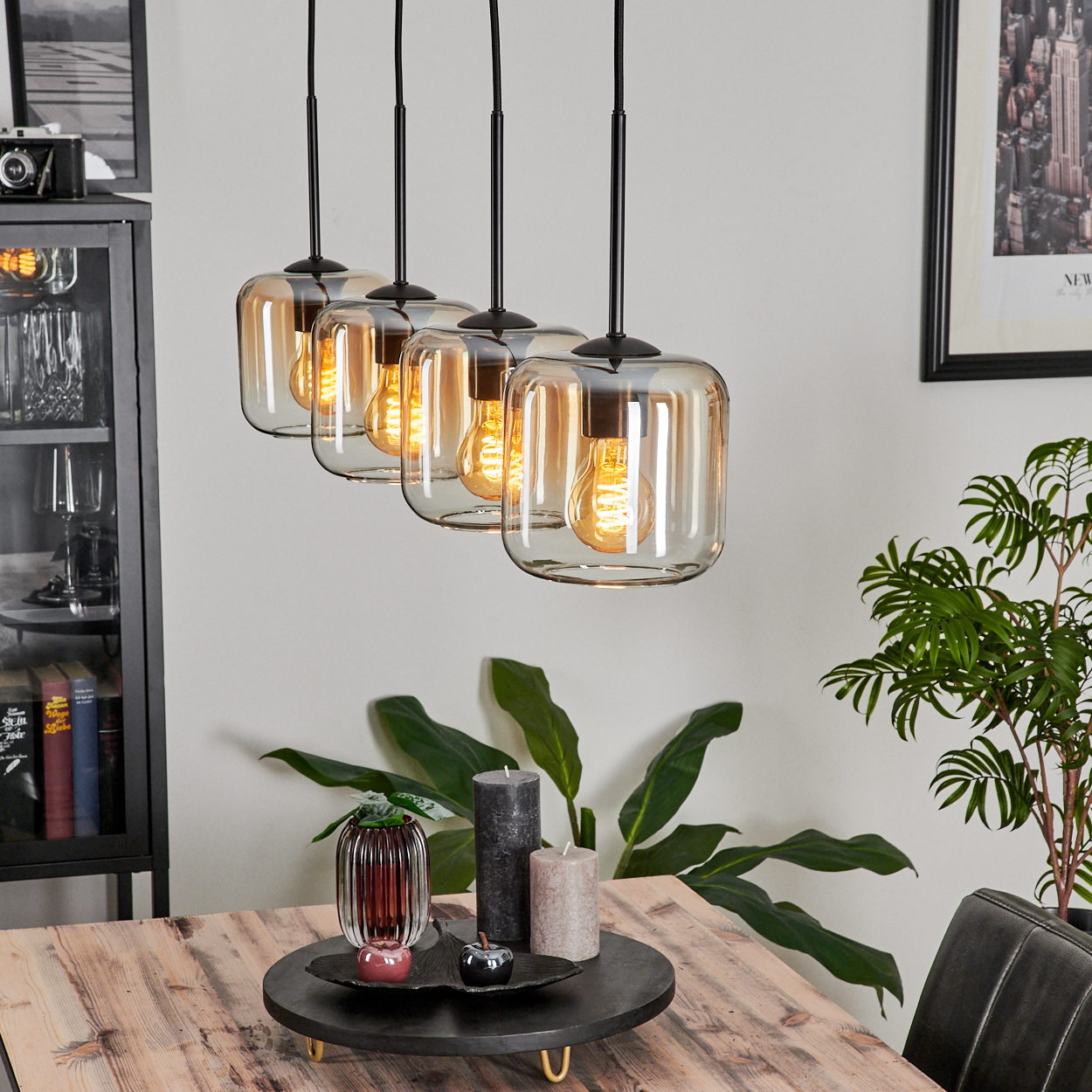 Esszimmer mit Holztisch, vier Pendelleuchten, Kerzen und anderer Dekoration, gemütliche Atmosphäre.