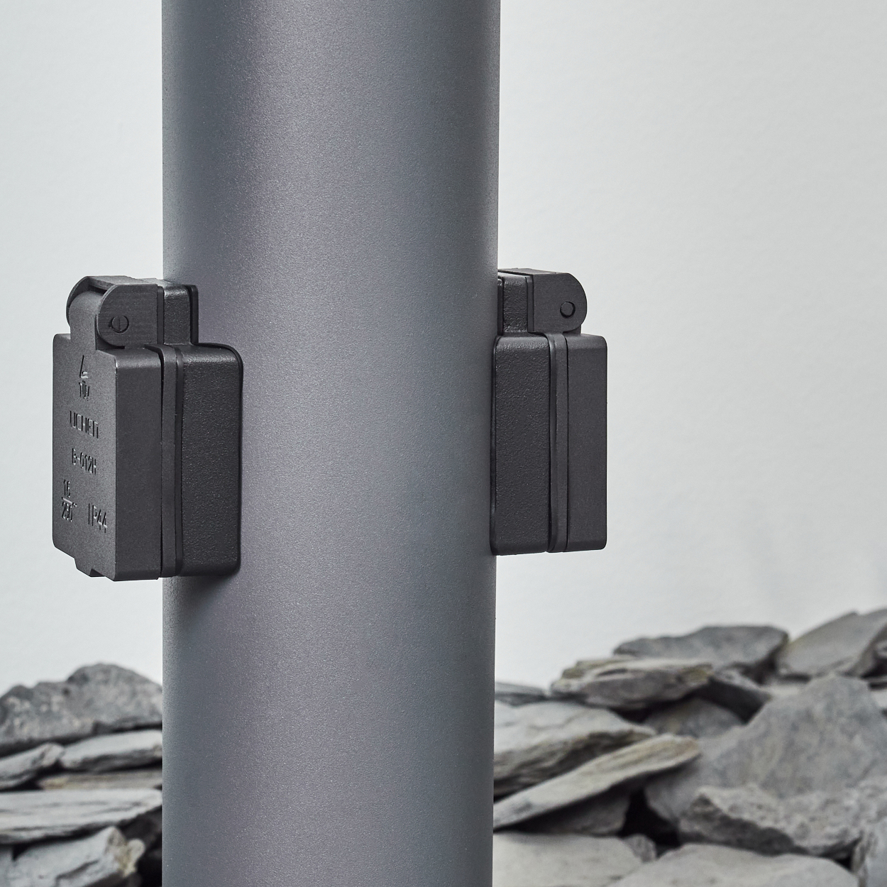 Nahaufnahme einer grauen Lampe mit zwei angebrachten schwarzen Kästen. Der Hintergrund ist grauer Stein.