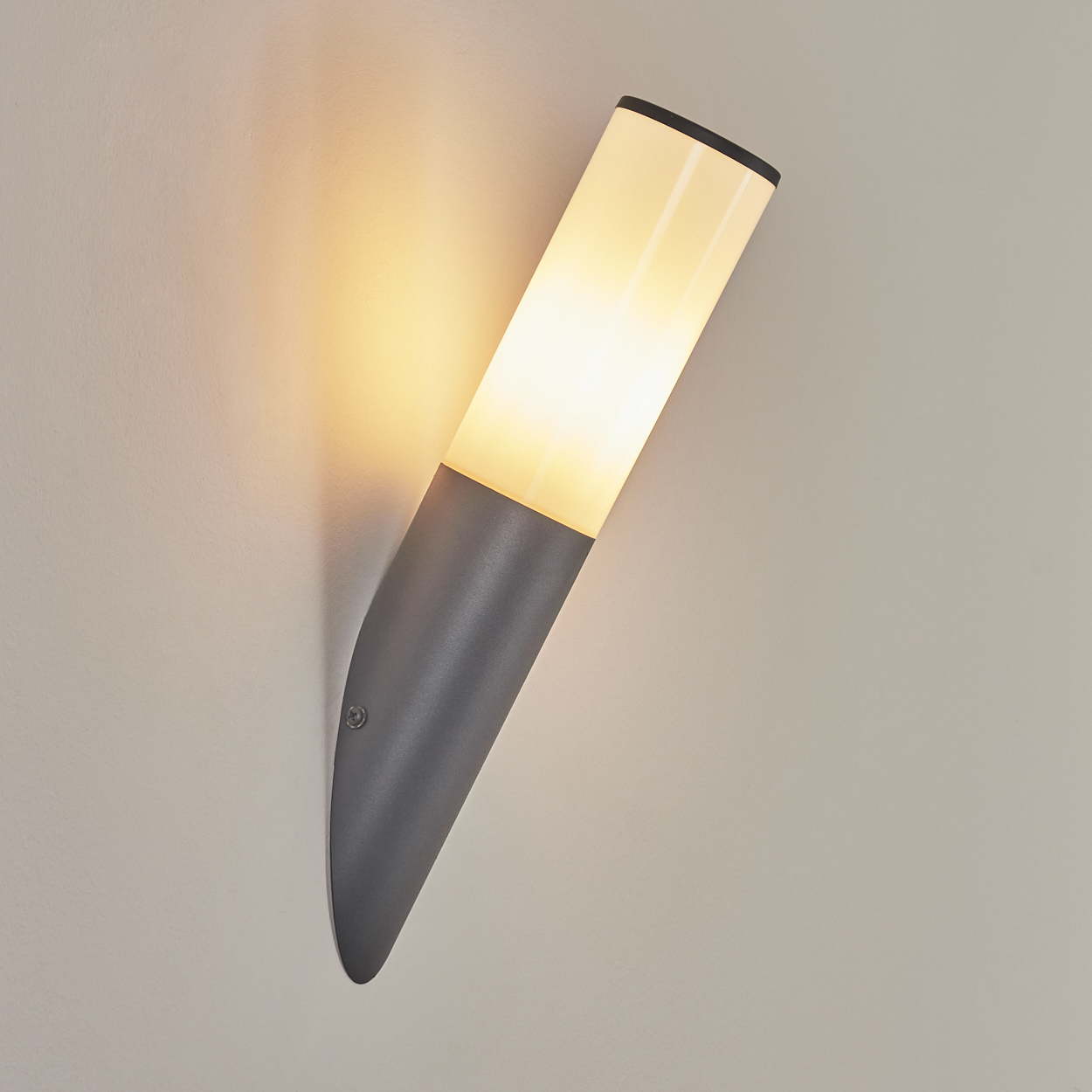 Graue Wandleuchte mit weißem Lichtteil und schwarzem Deckel. Schräge Ansicht an heller Wand.