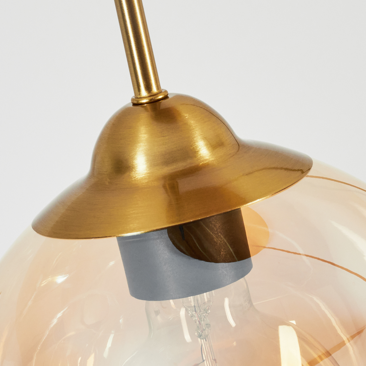 Nahaufnahme einer Glühbirne in einer Glaskugellampe mit goldfarbenem Aufsatz.