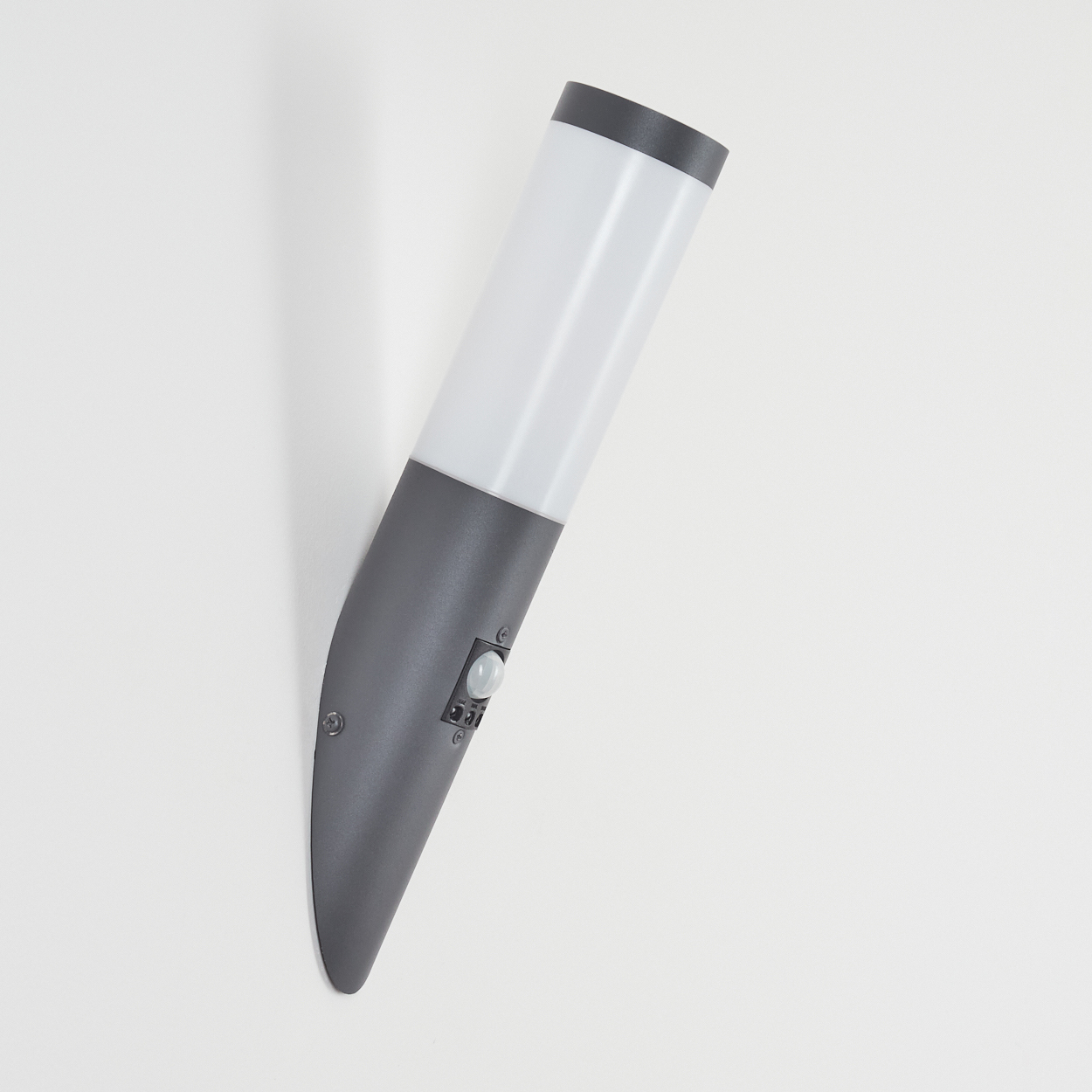 Graue Außenlampe an weißer Wand, zylindrische Form mit weißem Lichtpanel und Sensor.