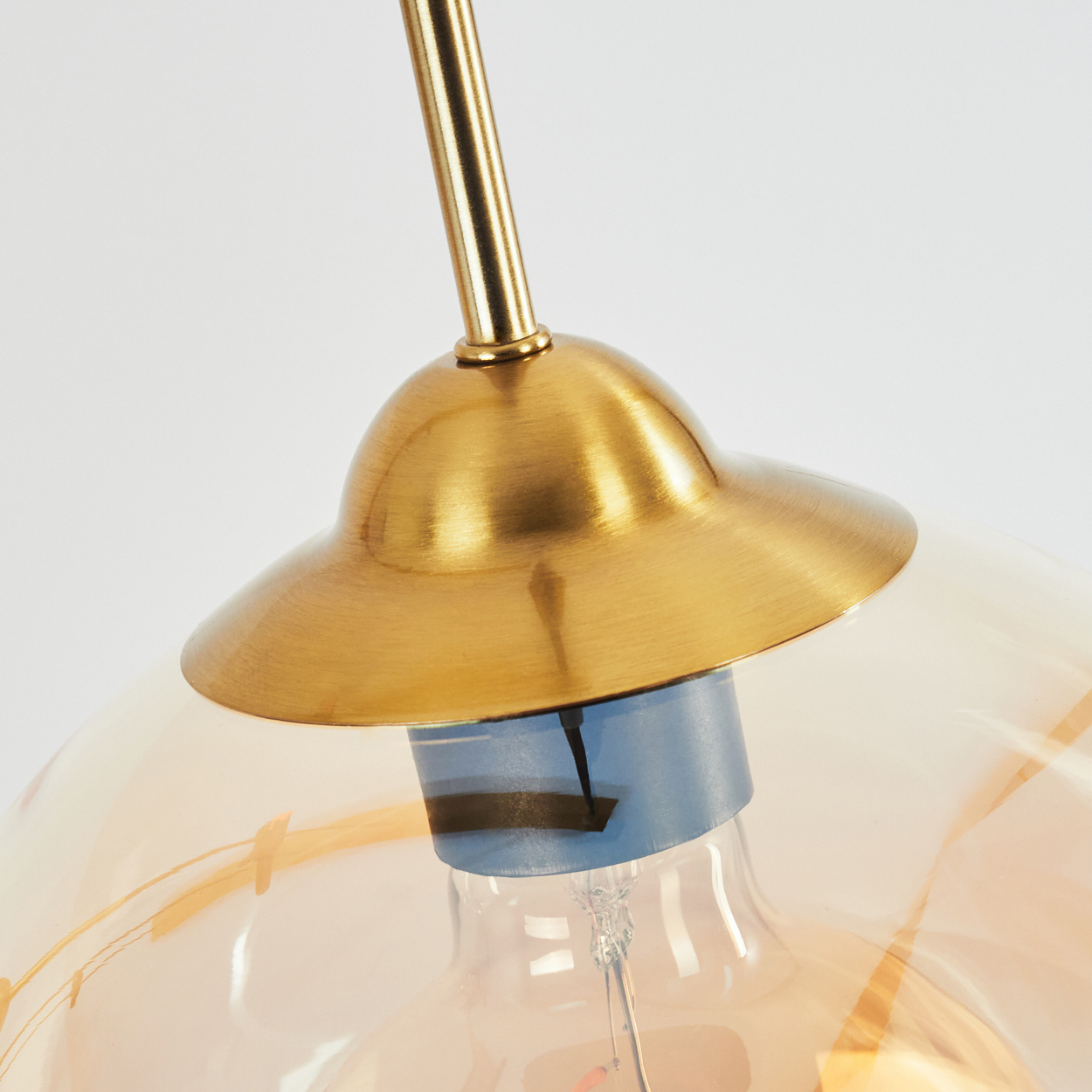 Nahaufnahme einer Hängeleuchte mit goldenen Akzenten, Glaskugelschirm und Edison-Glühbirne.
