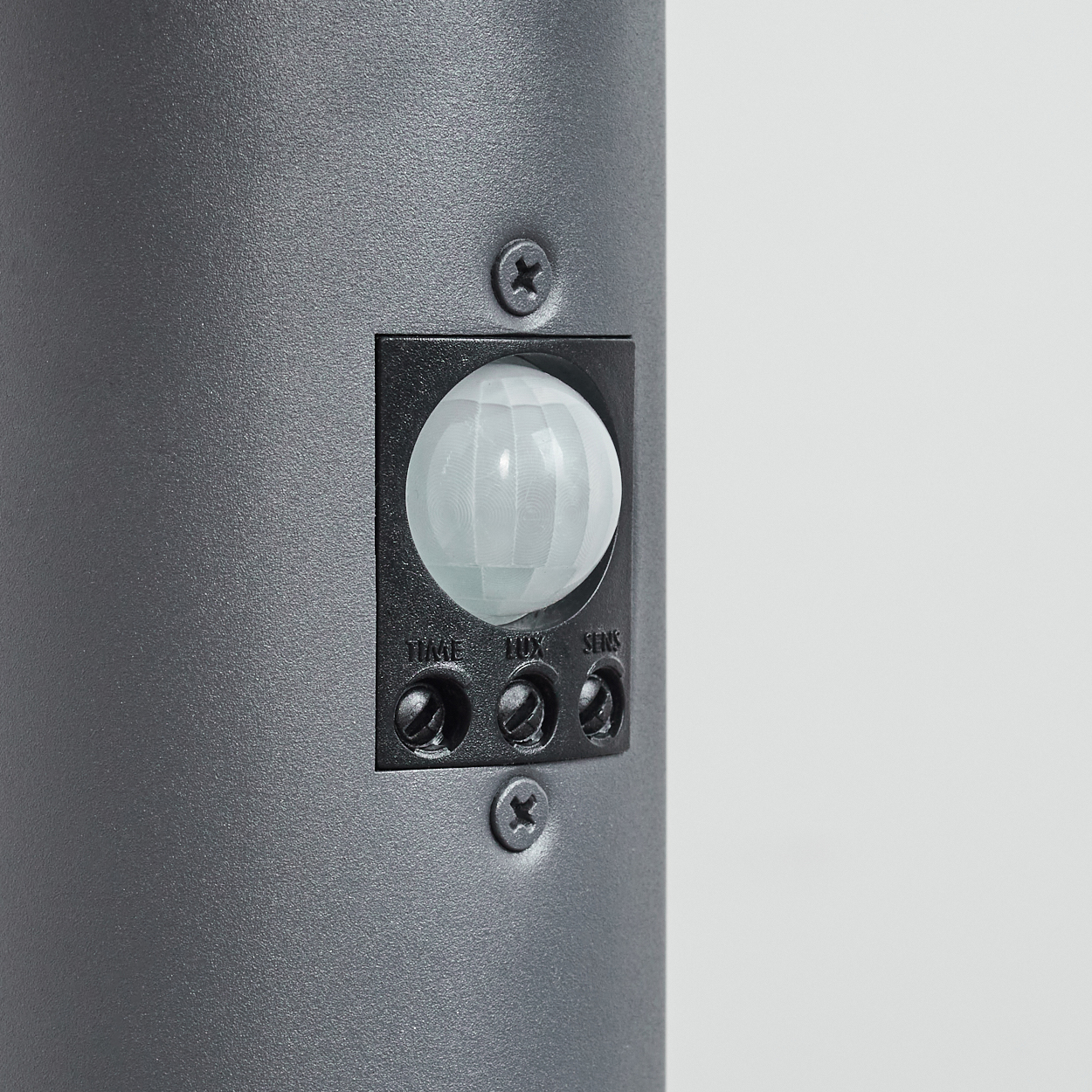 Nahaufnahme eines Bewegungssensors an einer grauen Säulenlampe. Es hat drei Einstellräder und einen runden Sensor.
