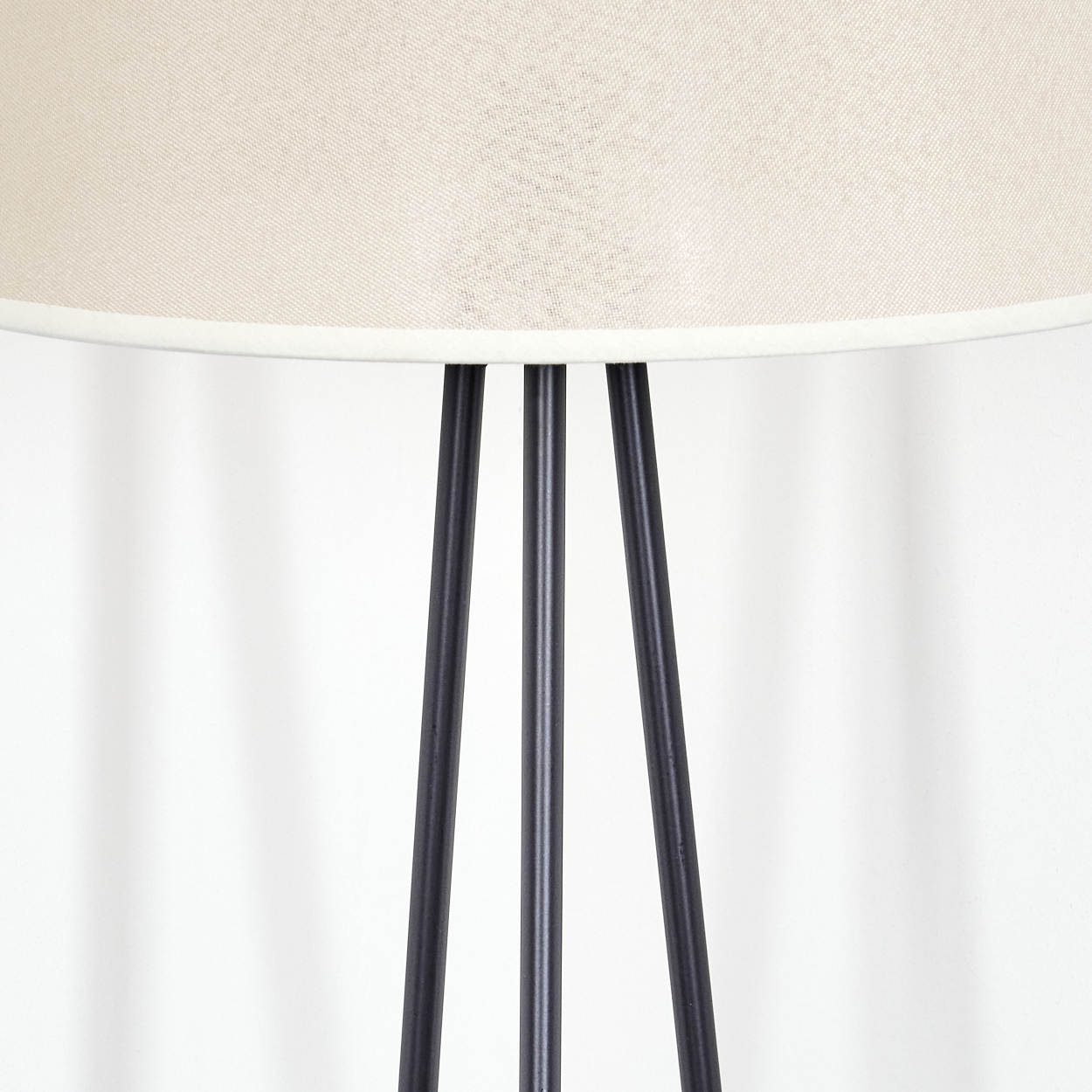 Nahaufnahme eines beigen Lampenschirms auf einer Stativlampe. Schwarze Metallbeine, weißer Hintergrund.