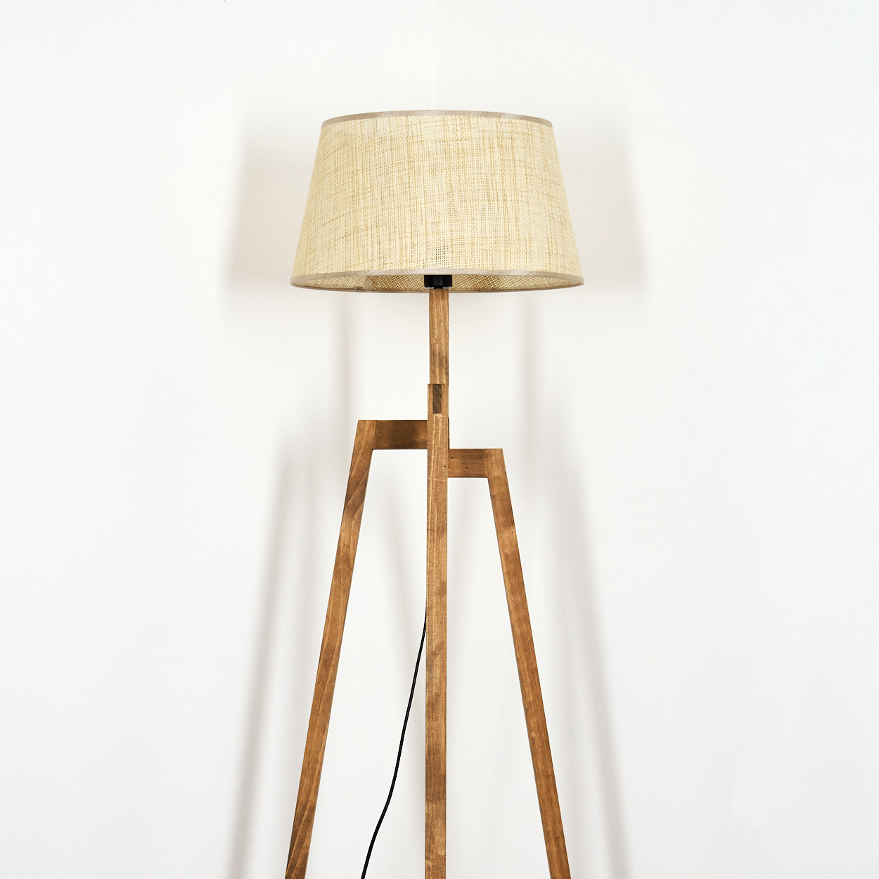 Holz-Stativlampe mit beigefarbenem Schirm vor weißer Wand.