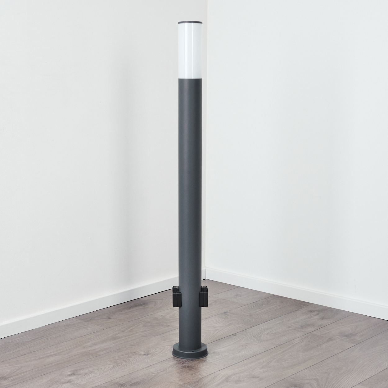 Grauer Außenmast mit weißem Licht. Der Hintergrund ist eine weiße Wand.