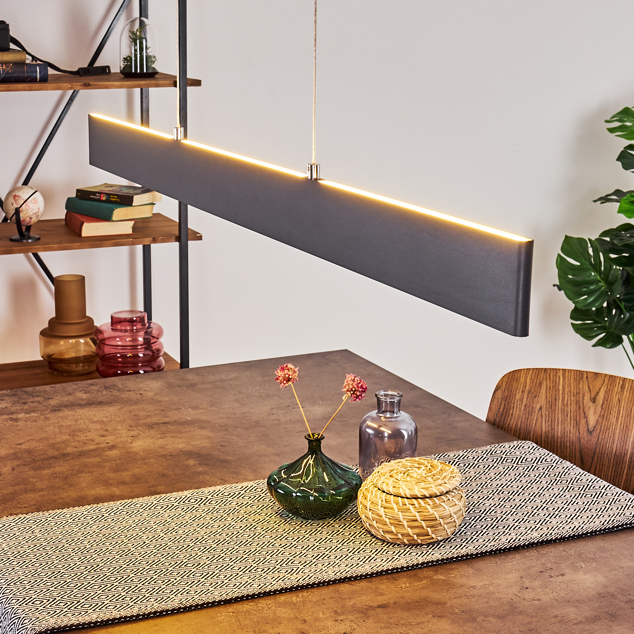 Hängende schwarze Leuchte über einem Holztisch. Enthält Vasen, Blumen und einen Tischläufer.