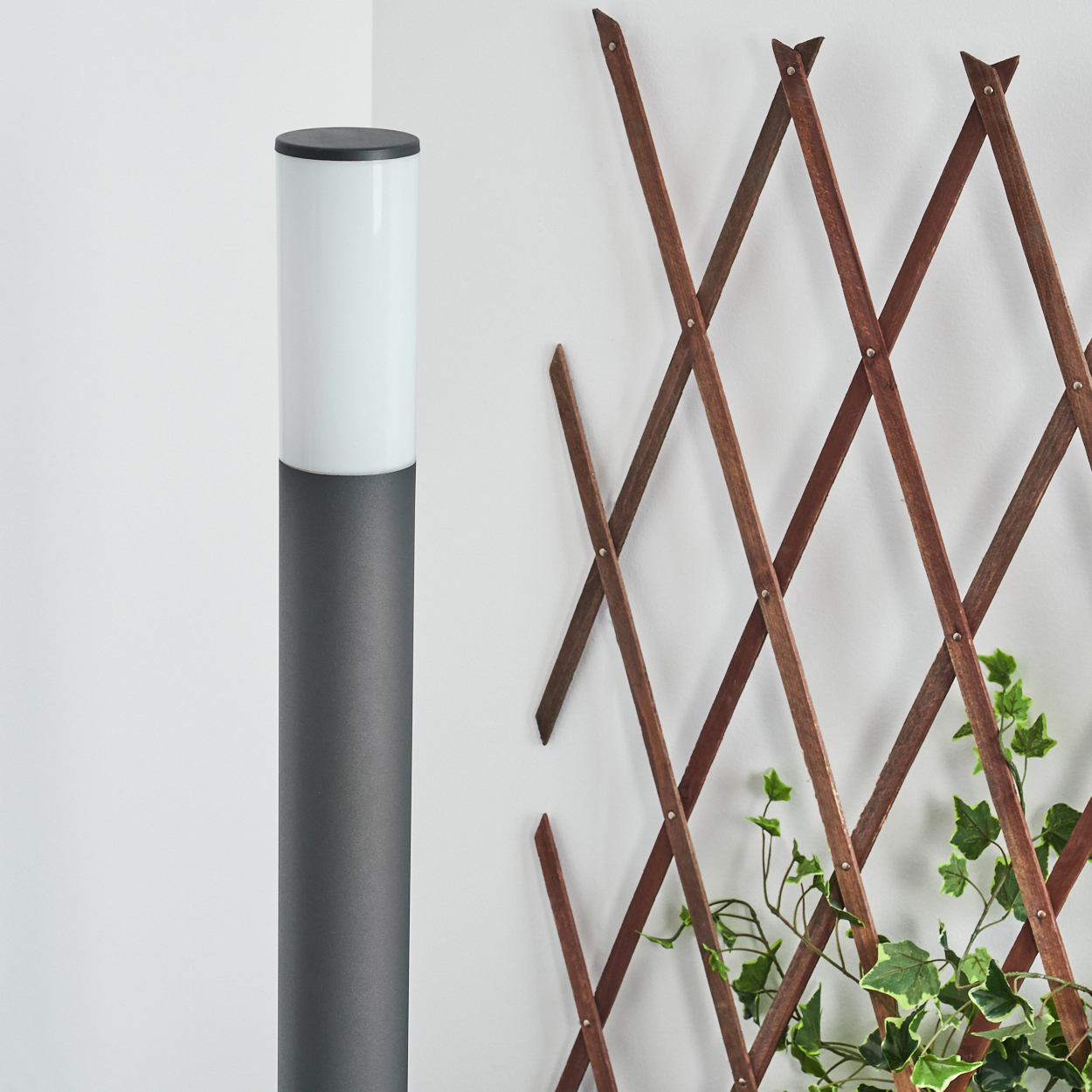Außenlampe, grau mit weißem Oberteil. Neben Holzgitter und Pflanzen.