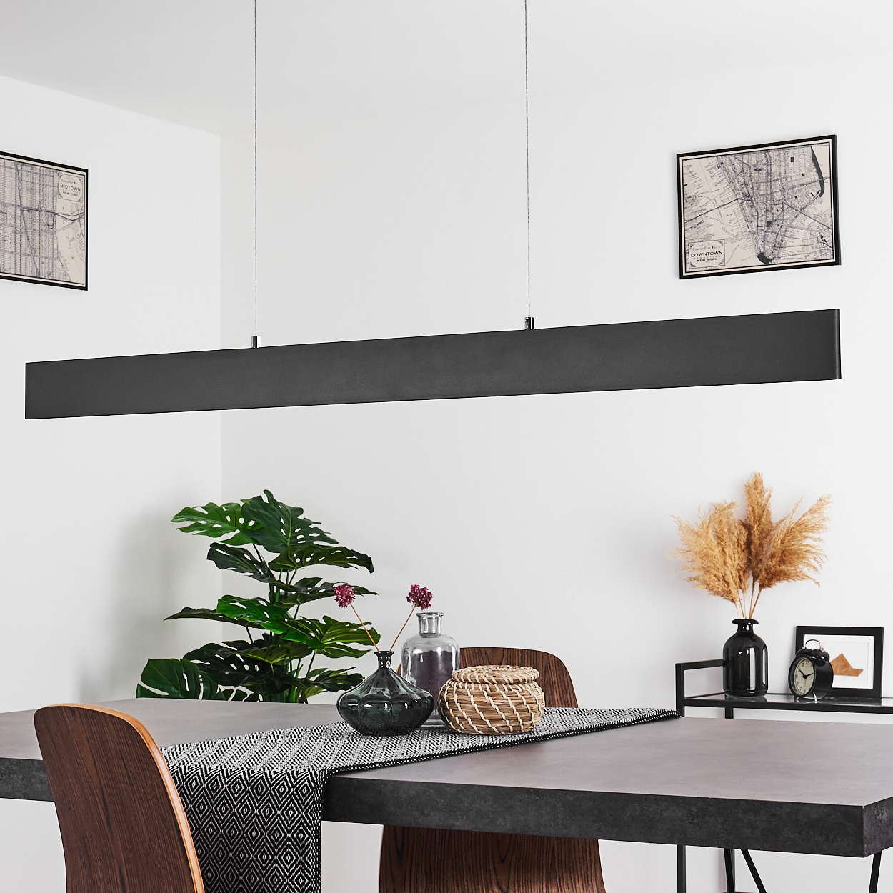 Lange, schwarze Leuchte über einem Tisch mit Esstisch, Karten und Pflanzen.
