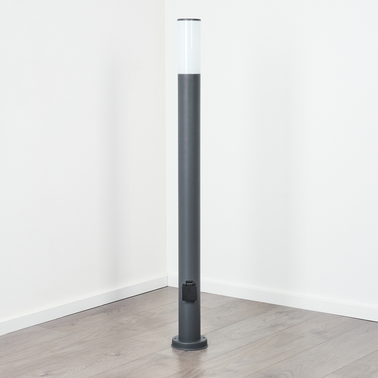 Hohe, graue Außenlampe auf weißem Hintergrund in einer Ecke, mit weißem und klarem Oberteil.