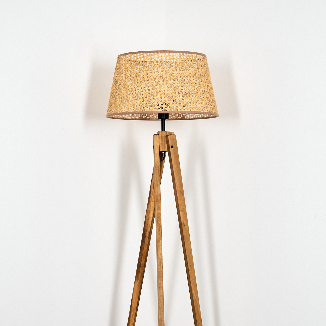 Stehlampe mit Holzstativ und gewebtem Lampenschirm vor weißer Wand. Sauberer, minimalistischer Stil.