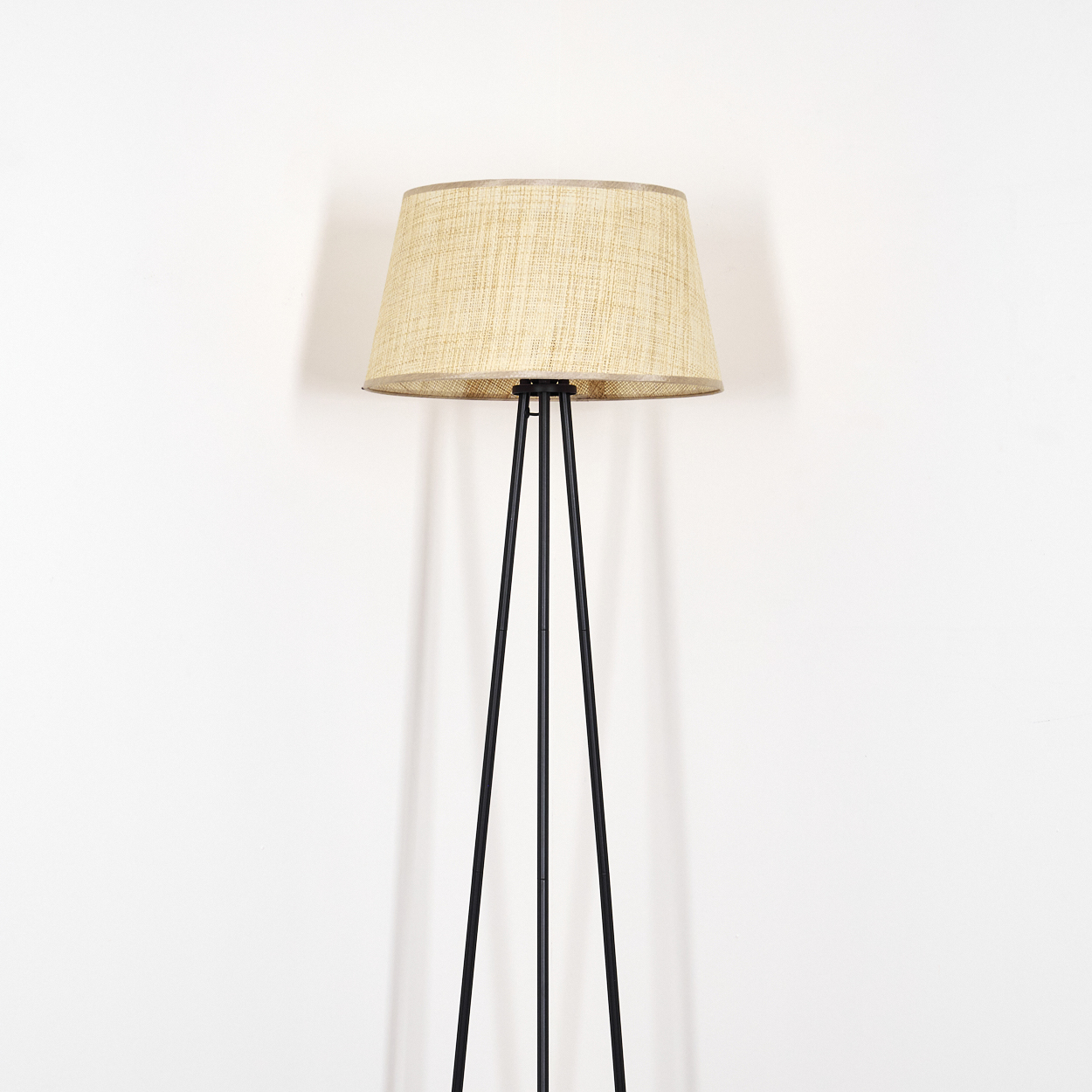 Eine hohe schwarze Stehlampe mit beigem Stoffschirm, vor weißem Hintergrund.